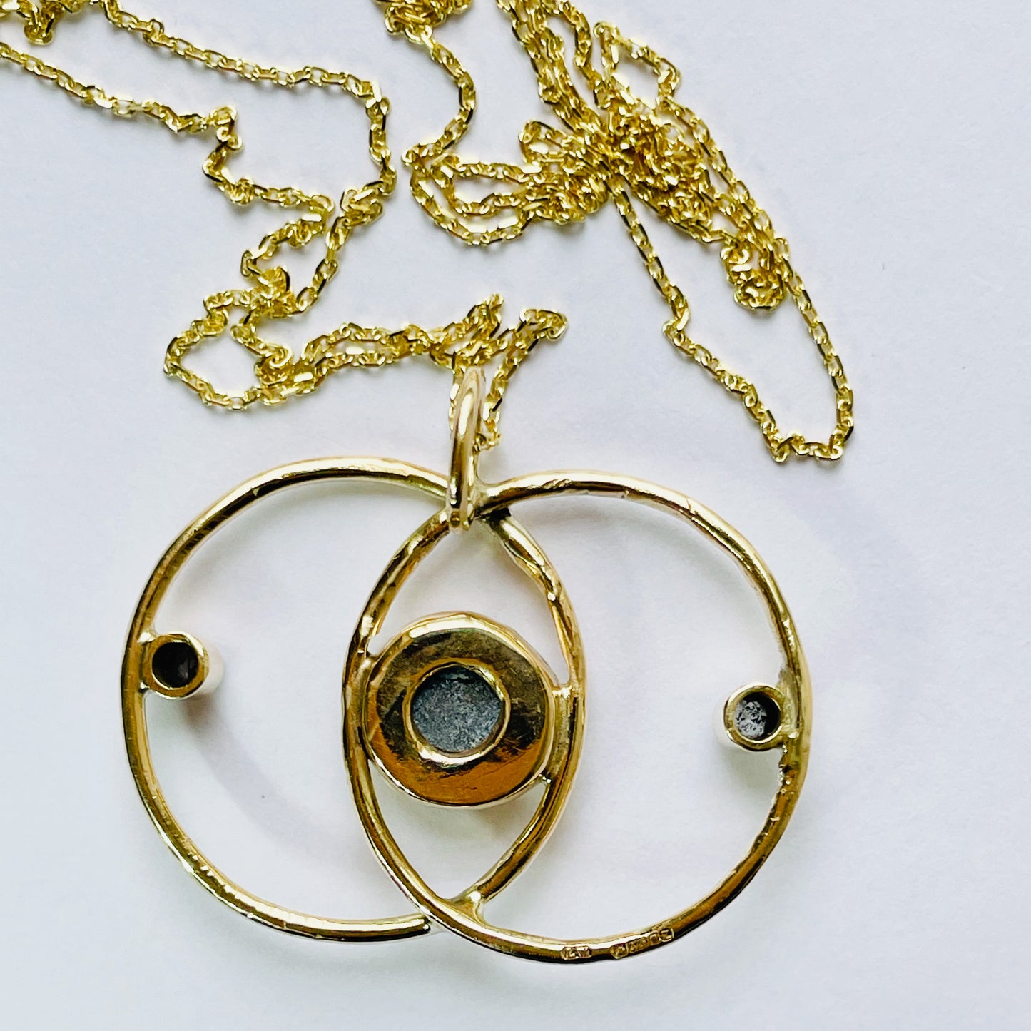 Expanded Skies Blue Sapphire Vesica Piscis Pendant has a large beautiful ethically sourced Sri Lankan blue sapphire with ripples of deep and paler blues, balanced by two faceted white sapphires. The pendent has a handcrafted sculpted and textured setting to reflect the undulating surface of cabochon cut sapphire, in lovely yellow recycled 9ct gold.