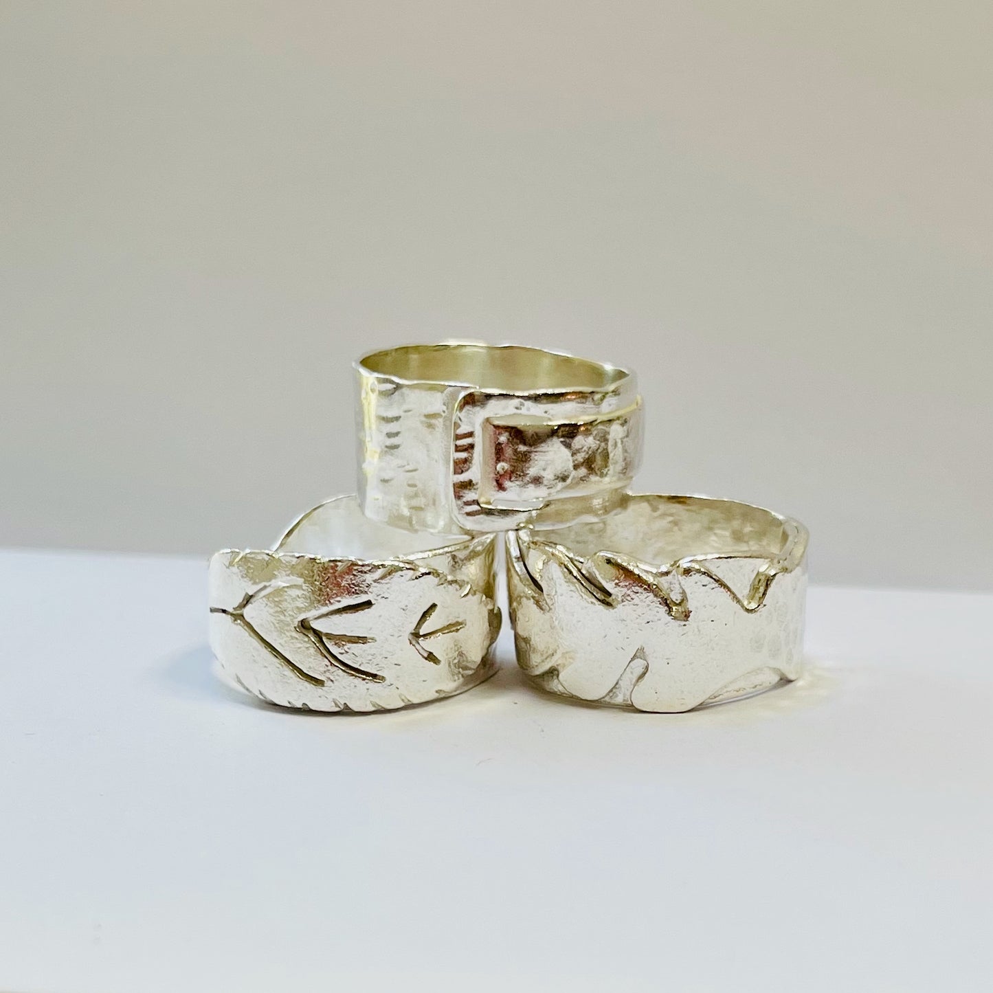 Expanded Skies Wide Ring Workshop Three silver rings with leaf and abstract designs on a light background