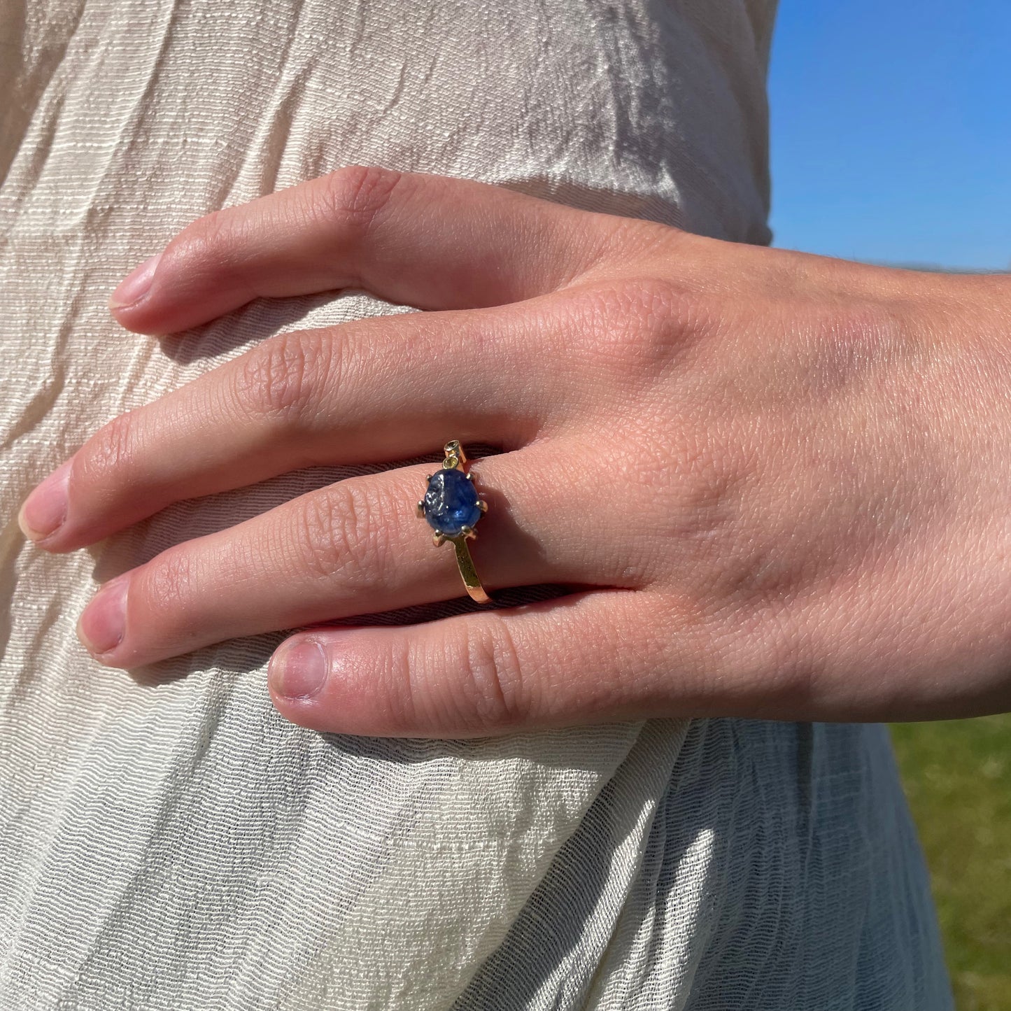 Close up with hand the Dartmoor Sun and Skies Sapphire Ring reflects the big Dartmoor skies, the contrasting colours and textures of the moving light over the landscape, created with ethically sourced raw and facetted sapphires and different shades of gold.