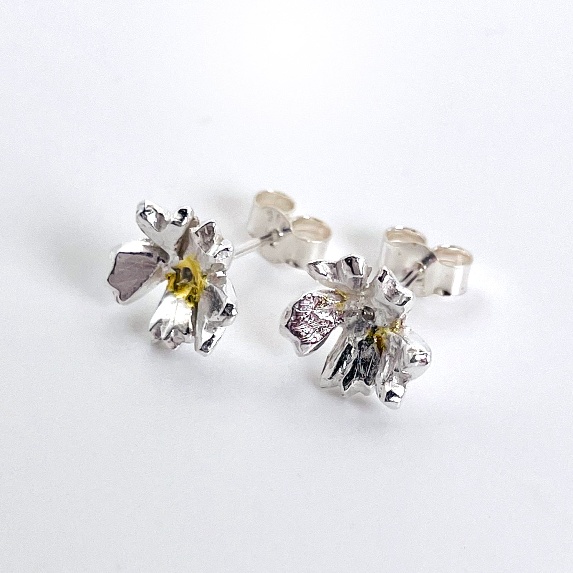 The Expanded Skies Dartmoor Field Rose Studs captures the joyous simple beauty of the field rose, Rosa arvensis, that is seen weaving brightly through the Dartmoor hedgerows and woodland.
Handcrafted in recycled fine silver with recycled 24ct gold accents and recycled sterling silver ear pins and scrolls.