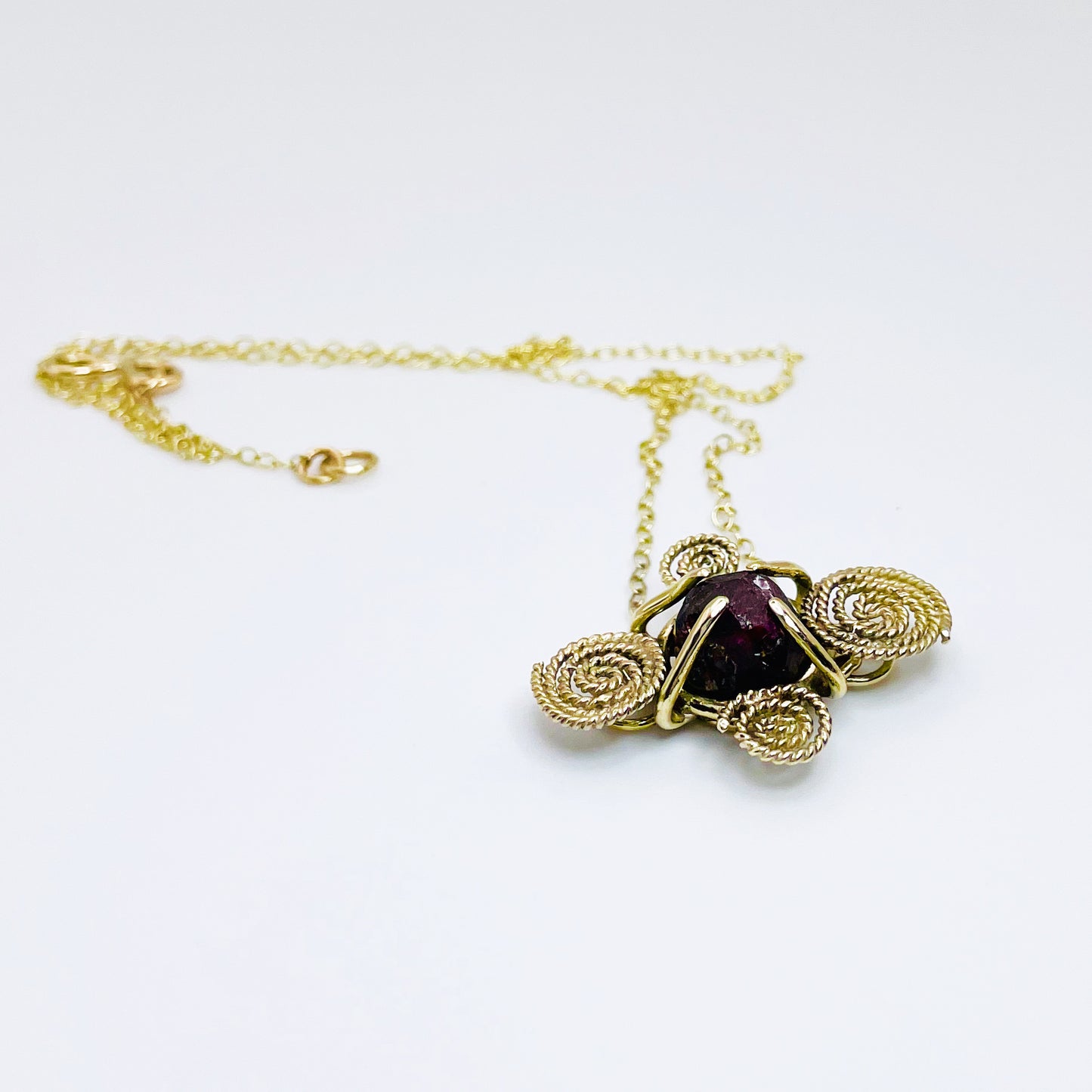 The Expanded Skies Raw Garnet Spiral Filigree Necklace has a beautiful raw Norwegian garnet set in 9ct gold. The garnet is set in a distinctive completely handcrafted 9ct gold filigree and claw setting. It features the neolithic symbol of the spiral, representing the life force and the cycles of life. This is a unique piece, one-of-a-kind. Handcrafted on the edge of Dartmoor and made from high quality recycled gold, Hallmarked by the London Assay Office.