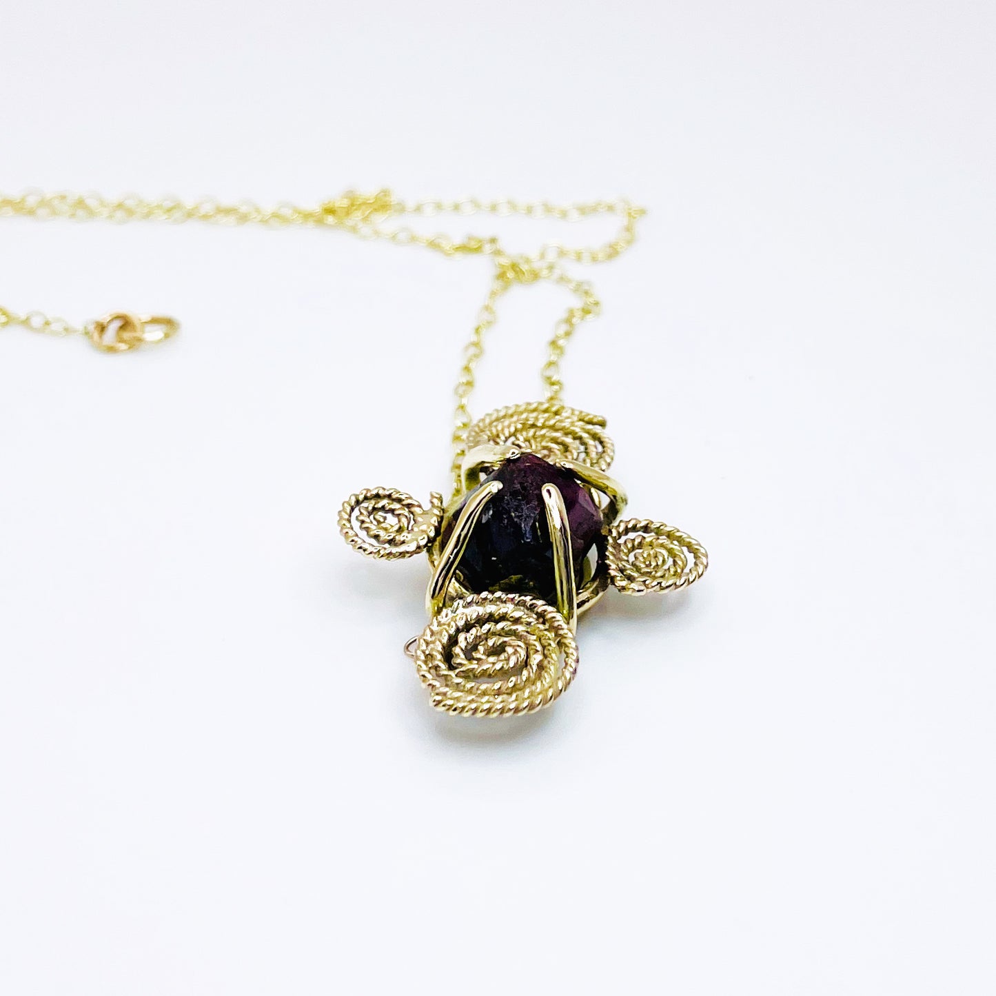 The Expanded Skies Raw Garnet Spiral Filigree Necklace has a beautiful raw Norwegian garnet set in 9ct gold. The garnet is set in a distinctive completely handcrafted 9ct gold filigree and claw setting. It features the neolithic symbol of the spiral, representing the life force and the cycles of life. This is a unique piece, one-of-a-kind. Handcrafted on the edge of Dartmoor and made from high quality recycled gold, Hallmarked by the London Assay Office.