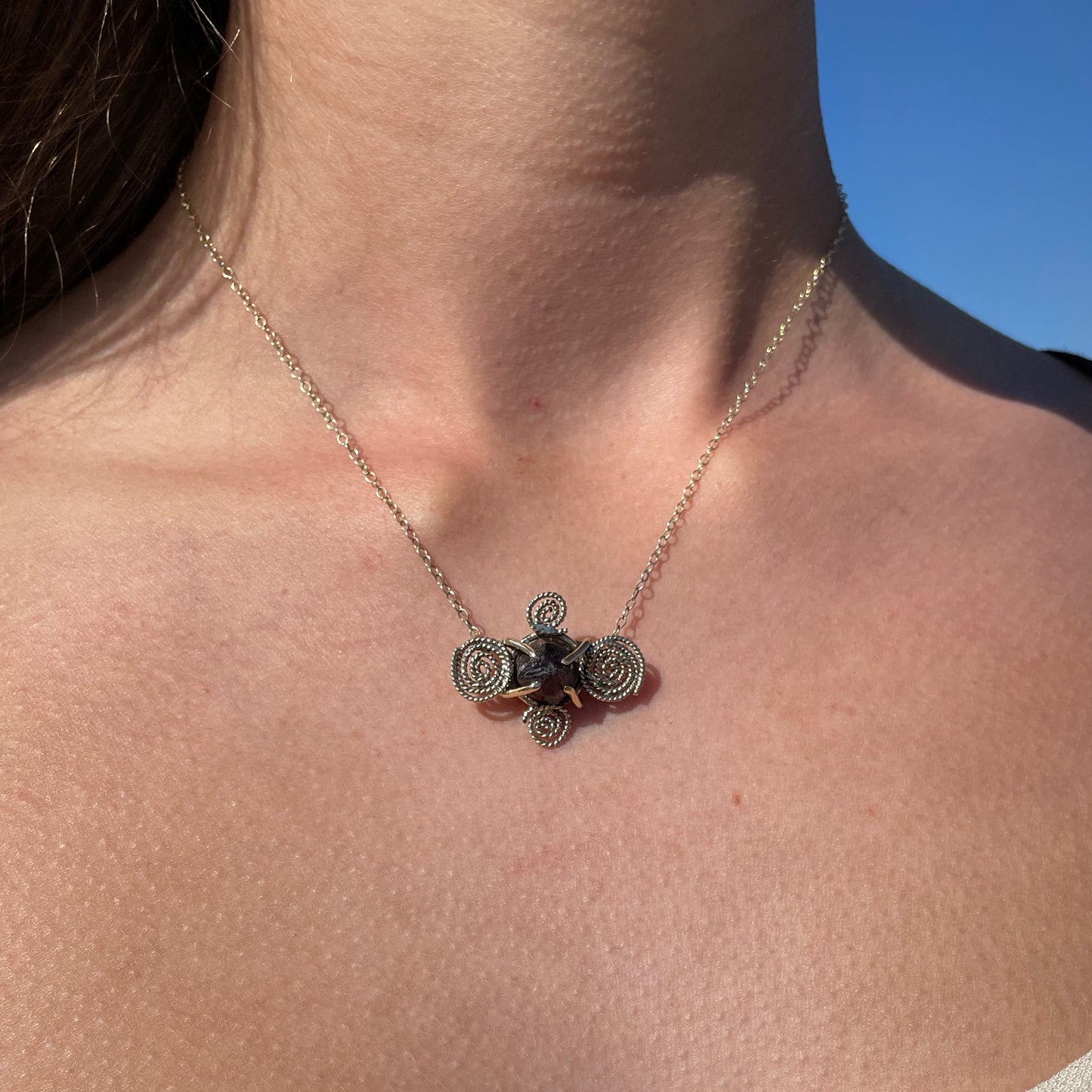 The Expanded Skies Raw Garnet Spiral Filigree Necklace has a beautiful raw Norwegian garnet set in 9ct gold. The garnet is set in a distinctive completely handcrafted 9ct gold filigree and claw setting. It features the neolithic symbol of the spiral, representing the life force and the cycles of life. This is a unique piece, one-of-a-kind. Handcrafted on the edge of Dartmoor and made from high quality recycled gold, Hallmarked by the London Assay Office.