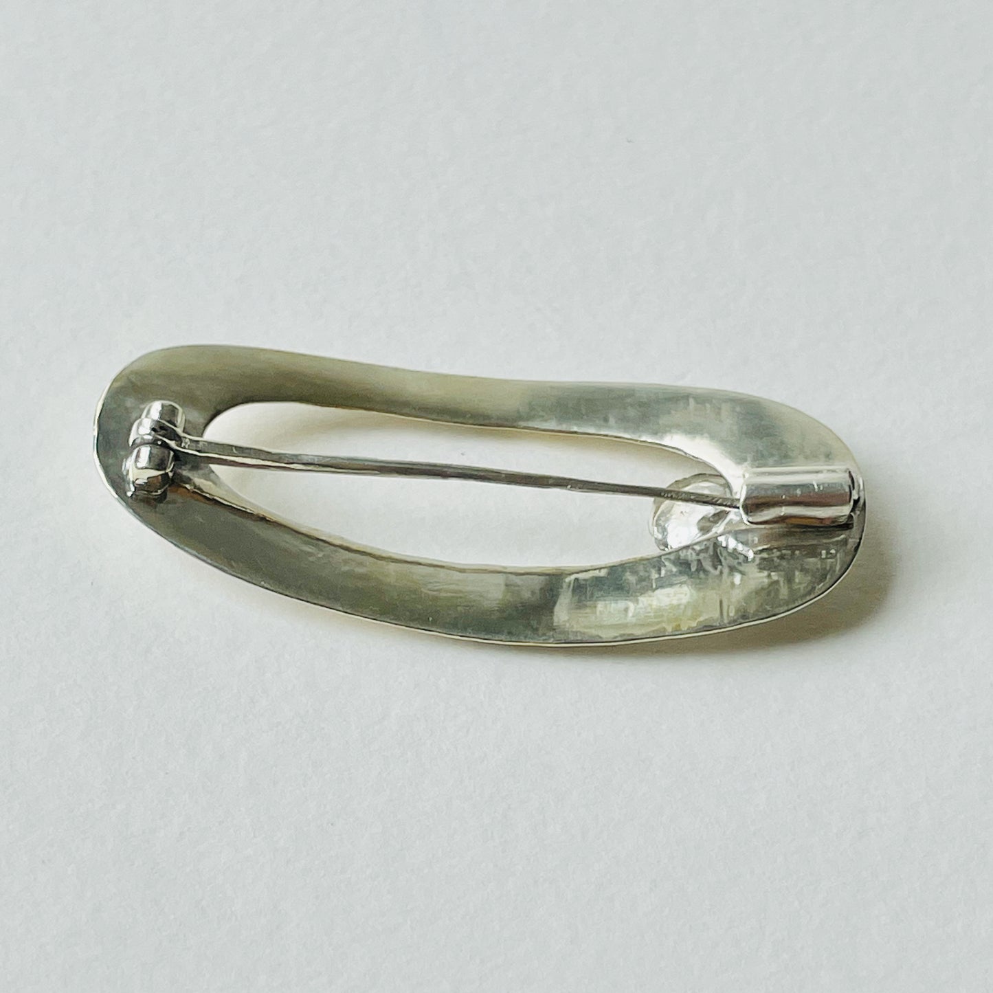 The River Dart at Hembury Brooch is inspired by eddies that glint as they swirl around rocks and tiny islands. The brooch is made from recycled sterling silver that is etched, layered and inlaid with 9ct gold. Totally handcrafted, it has a beautiful 2mm ethically mined teal blue Sri Lankan sapphire set in 9ct recycled gold.