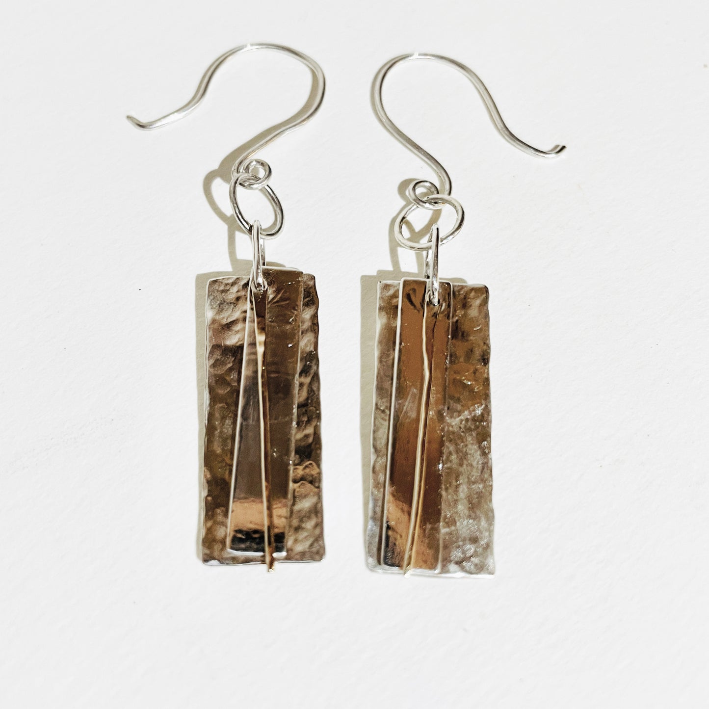 The Dartmoor Dart Valley earrings, are inspired by the River Dart, that viewed from high on top of granite moorland, glints and snakes through the steep sides of the deeply wooded valley. Handcrafted layers of solid recycled sterling silver are hammered and polished with a fine 9ct gold bar, that swing and catch the light.