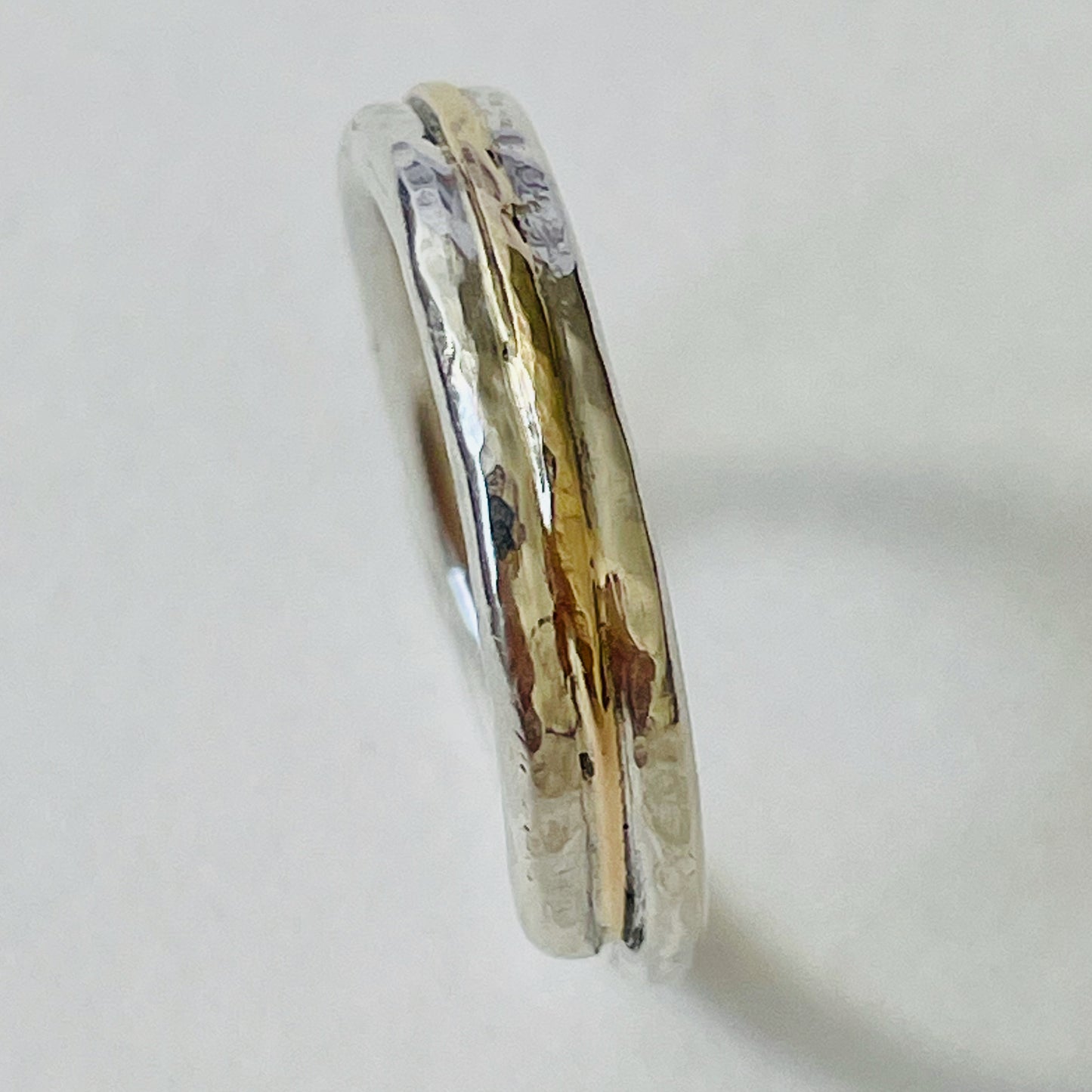 The Dartmoor Dart Valley Hammered Ring, inlaid with 9ct Gold, is inspired by the River Dart, that viewed from high on top of granite moorland, glints and snakes through the steep sides of the deeply wooded valley. The hammered band is handcrafted from a single band of sold sterling recycled silver at back that flows into a recycled 9ct gold band at the front, flanked by two silver bands. Wear everyday, perfect as a wedding ring or to accompany any outfit, understated, beautiful.