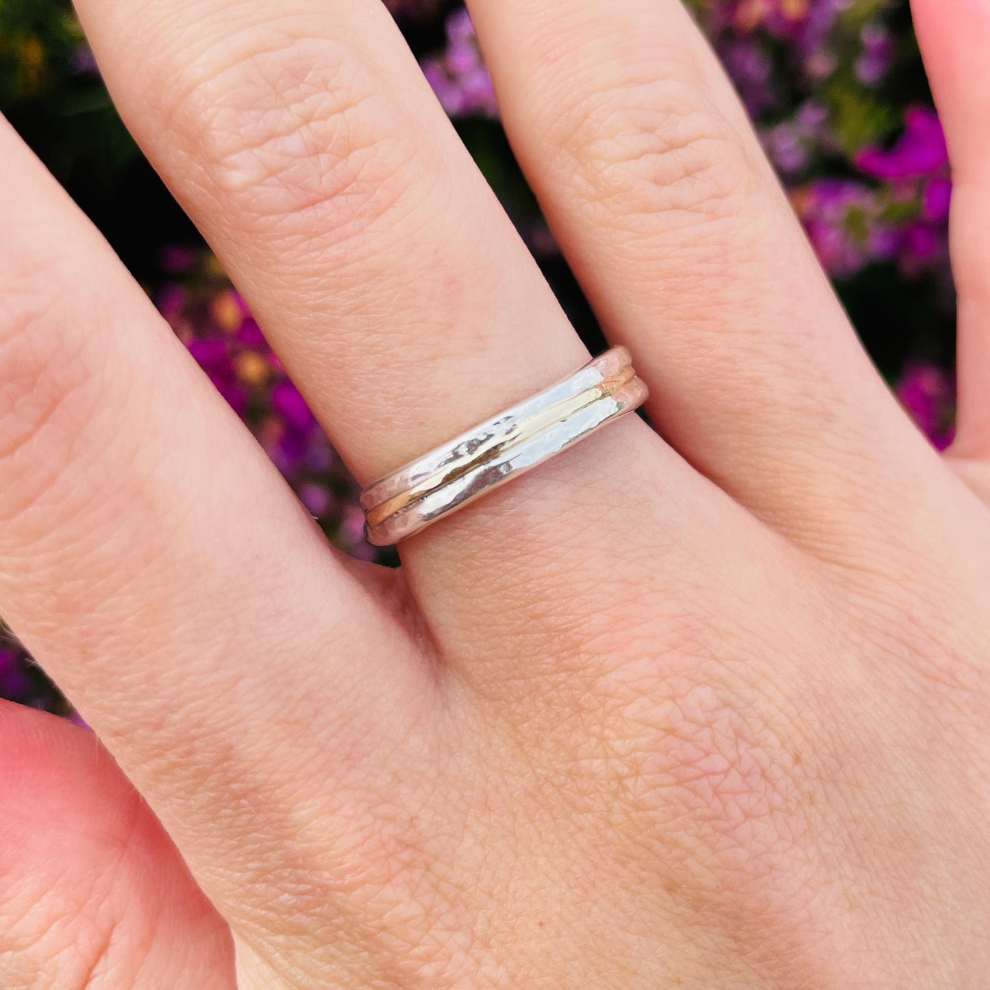 woman wearing The Dartmoor Dart Valley Hammered Ring, inlaid with 9ct Gold, is inspired by the River Dart, that viewed from high on top of granite moorland, glints and snakes through the steep sides of the deeply wooded valley. The hammered band is handcrafted from a single band of sold sterling recycled silver at back that flows into a recycled 9ct gold band at the front, flanked by two silver bands. Wear everyday, perfect as a wedding ring or to accompany any outfit, understated, beautiful.