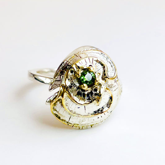 The Hembury Castle Ring design is based on archaeological remains of the mott and bailey Norman castle in Hembury Woods, on the edge of Dartmoor. It is created with hand engraving, inlaid with 9ct gold and set with a beautiful 3mm brilliant cut green Australian sapphire, ethically sourced from Nineteen48. The 'secret' underside of the ring has the symbol of for non-coniferous woodland.