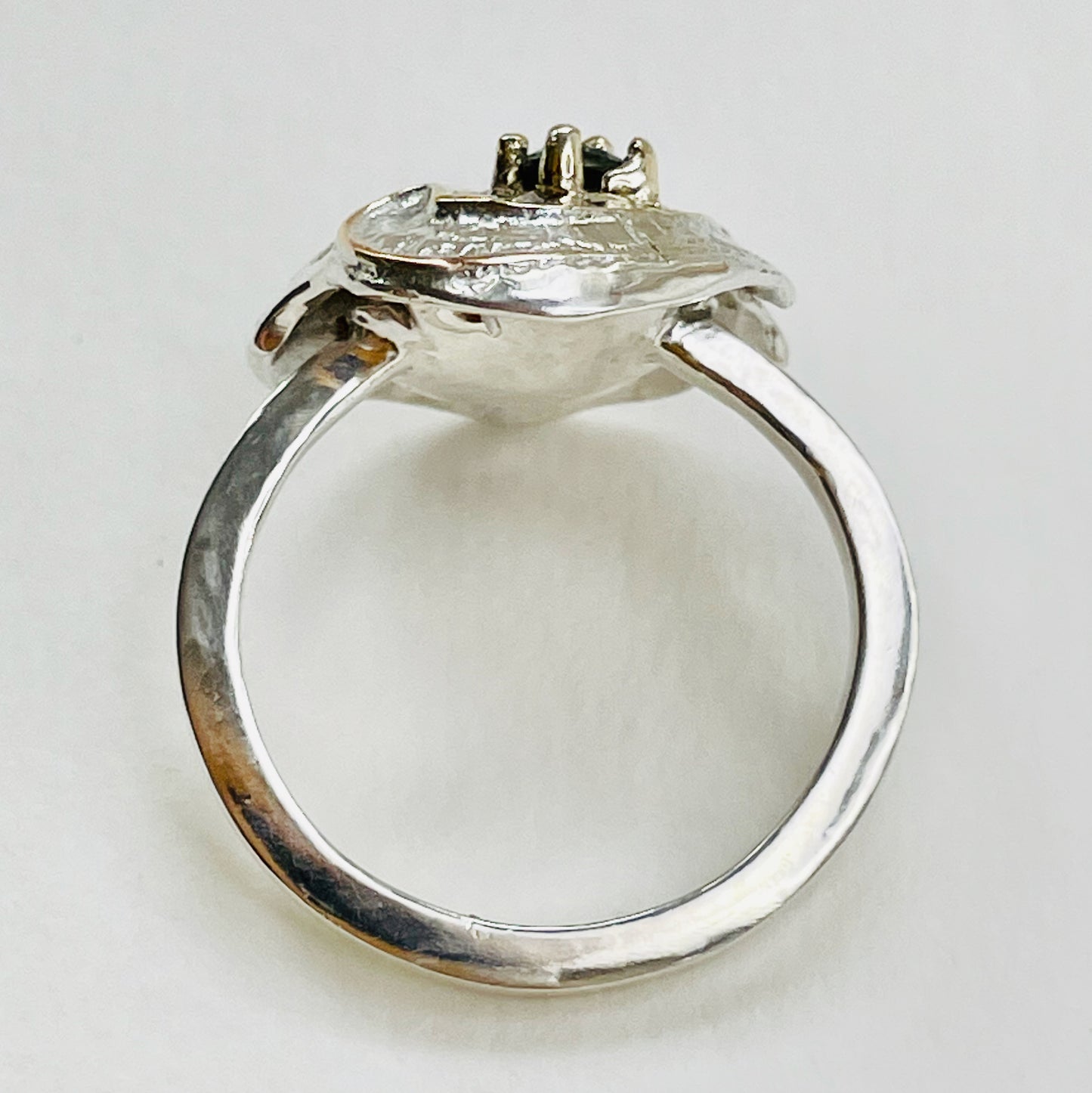 he Hembury Castle Ring design is based on archaeological remains of the mott and bailey Norman castle in Hembury Woods, on the edge of Dartmoor. It is created with hand engraving, inlaid with 9ct gold and set with a beautiful 3mm brilliant cut green Australian sapphire, ethically sourced from Nineteen48. The 'secret' underside of the ring has the symbol of for non-coniferous woodland.