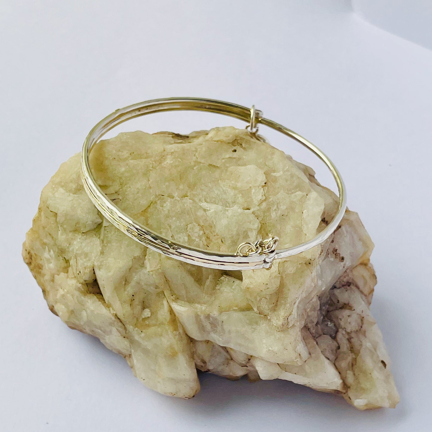 The Hembury Woods Hinged Bangle evokes the river Dart River at Hembury, where the water eddies and glints as it swirls around the rocks. Silver is formed to reflect the undulating river course and the glinting water, inlaid with 9ct gold. The bangle is totally handcrafted on the edge of Dartmoor and made from high quality recycled sterling silver, and recycled 9ct gold and with a textured hammered finish that reflects the light. Understated and beautiful, it can be worn every day. It can be personalised.