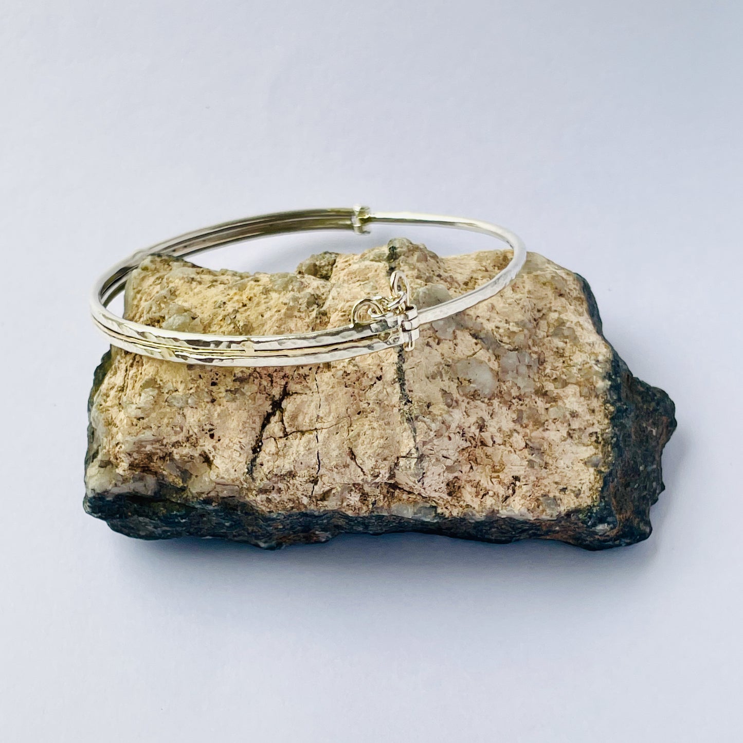 The Hembury Woods Hinged Bangle evokes the river Dart River at Hembury, where the water eddies and glints as it swirls around the rocks. Silver is formed to reflect the undulating river course and the glinting water, inlaid with 9ct gold. The bangle is totally handcrafted on the edge of Dartmoor and made from high quality recycled sterling silver, and recycled 9ct gold and with a textured hammered finish that reflects the light. Understated and beautiful, it can be worn every day. It can be personalised.