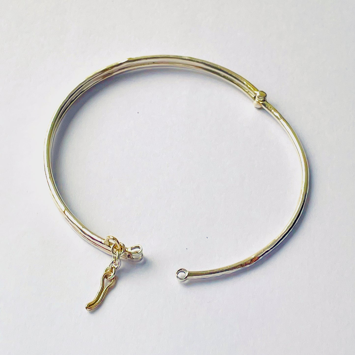 The Hembury Woods Hinged Bangle evokes the river Dart River at Hembury, where the water eddies and glints as it swirls around the rocks. Silver is formed to reflect the undulating river course and the glinting water, inlaid with 9ct gold. The bangle is totally handcrafted on the edge of Dartmoor and made from high quality recycled sterling silver, and recycled 9ct gold and with a textured hammered finish that reflects the light. Understated and beautiful, it can be worn every day. It can be personalised.