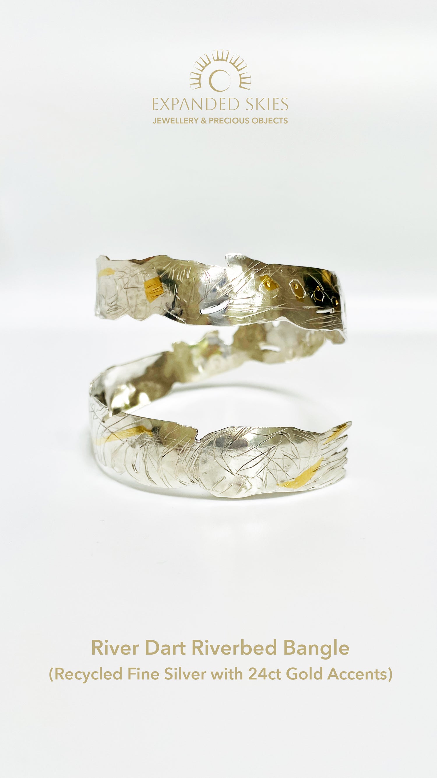 Expanded Skies River Dart Riverbed Bangle. The intricate patterns created by the River Dart moving over the riverbed shallows are the inspiration for the bangle’s form and the sketch-style hand engraving. The 24ct gold accents capture the sun moving over the water.
Specifications:
Made with recycled precious metals. Fine silver with hand engraving and 24ct gold accents, applied using the keum boo gilding process.
Handcrafted on the edge of Dartmoor in Emma Whittaker’s workshop. Hallmarked by the London