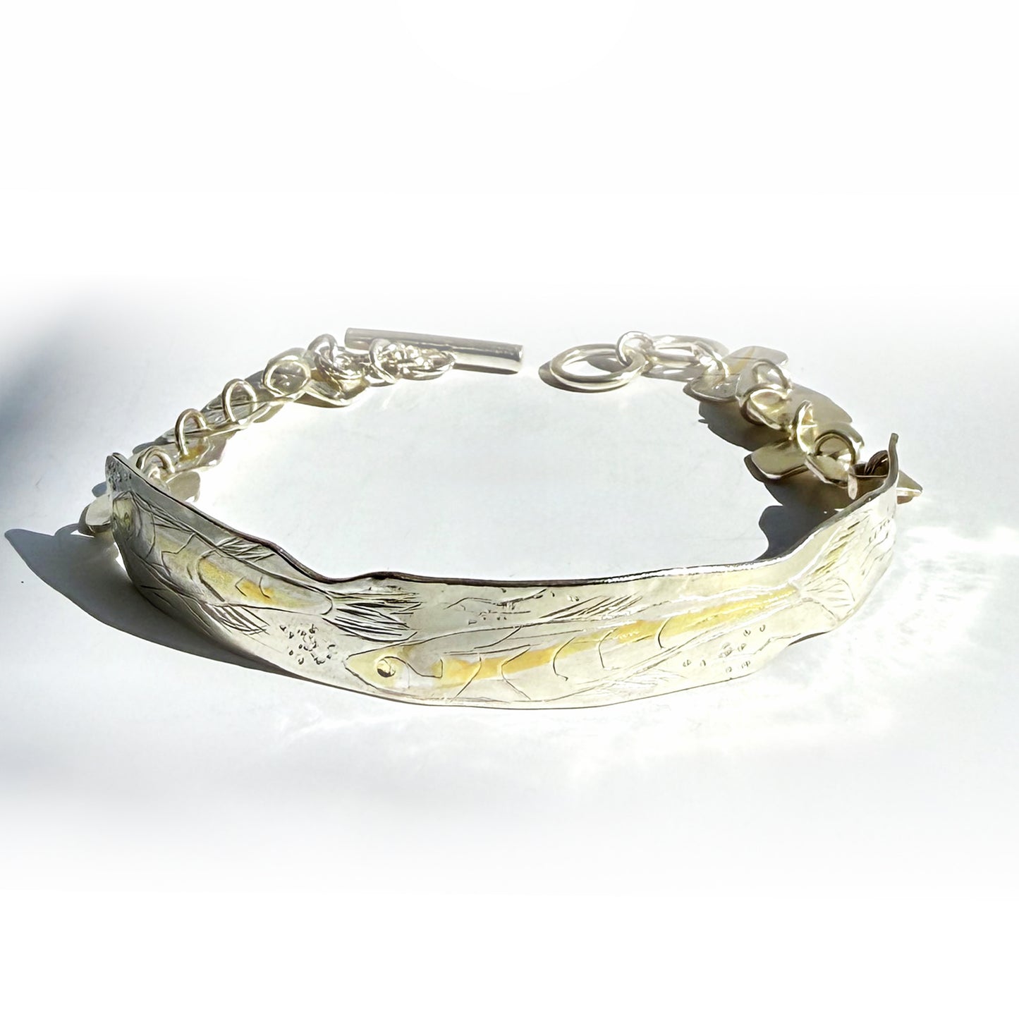 he Expanded Skies Dartmoor minnows bracelet captures the graceful beauty of the minnows as they somersault through the glistening River Dart at Hembury Woods, created in fine and sterling silver with 24ct gold accents. The chain is created with hand engraved fine silver panels with 24ct gold accents depict the moving river. Understated and beautiful, it can be worn every day or for special occasions, for men and women.The bracelet is totally handcrafted on the edge of Dartmoor from recycled precious metals