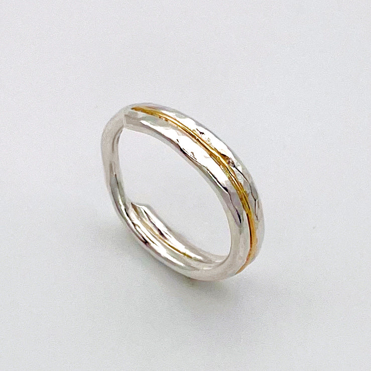 The Expanded Skies Dartmoor Dart Valley Hammered Ring, inlaid with 9ct Gold, is inspired by the River Dart, that viewed from high on top of granite moorland, glints and snakes through the steep sides of the deeply wooded valley. The hammered band is handcrafted from a single band of sold sterling recycled silver at back that flows into a recycled 9ct gold band at the front, flanked by two silver bands.