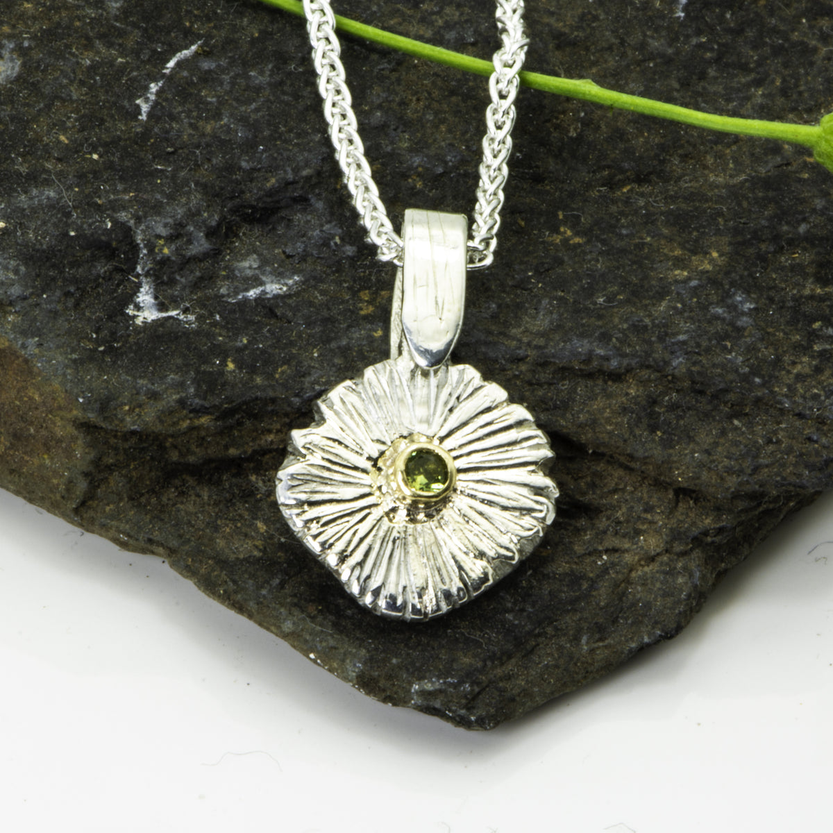 The Expanded Skies Dartmoor Green Daisy Sapphire Necklace in sterling silver and 9ct gold is inspired by the Erigeron Karvinskianus, commonly known as the 'Dartmoor Daisy'. It comes with 16” Italian spiga rolled chain, made from recycled sterling silver. The daisy pendant measures 12mm, the bail measures 6mm, total length 18mm with a depth of 2mm (approx). Each piece is individually saw pierced, hand engraved and
unique. The ethically sourced 2.5mm green sapphire is from Queensland, Australia.
