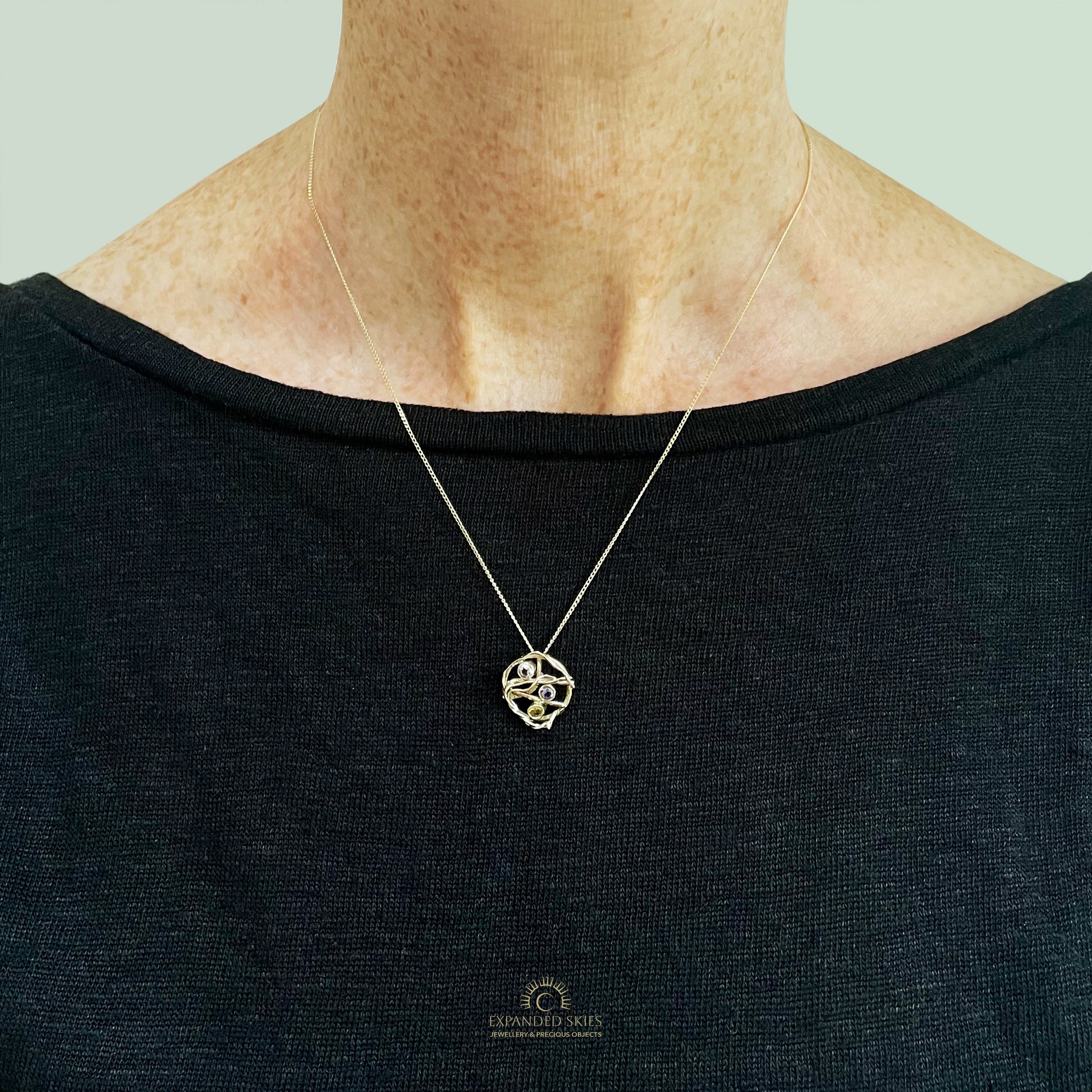 The Expanded Skies Haytor Heather and Gorse Amethyst and Sapphire Pendant evokes the beautiful yellows of the gorse and purples of the heather with an ethically sourced yellow sapphire and two amethysts held in twisting branches of 9ct yellow gold. The pendant comes with a 9ct gold chain, a choice of lengths are available, 16inch chain pictured on person