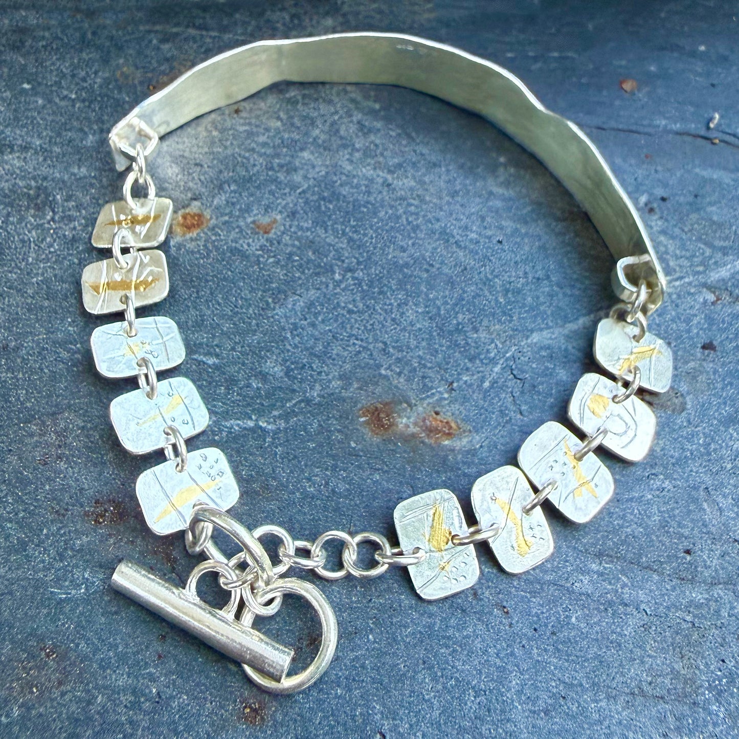 The Expanded Skies Dartmoor minnows bracelet captures the graceful beauty of the minnows as they somersault through the glistening River Dart at Hembury Woods, created in fine and sterling silver with 24ct gold accents. The chain is created with hand engraved fine silver panels with 24ct gold accents depict the moving river. Understated and beautiful, it can be worn every day or for special occasions, for men and women.The bracelet is totally handcrafted on the edge of Dartmoor from recycled precious metals