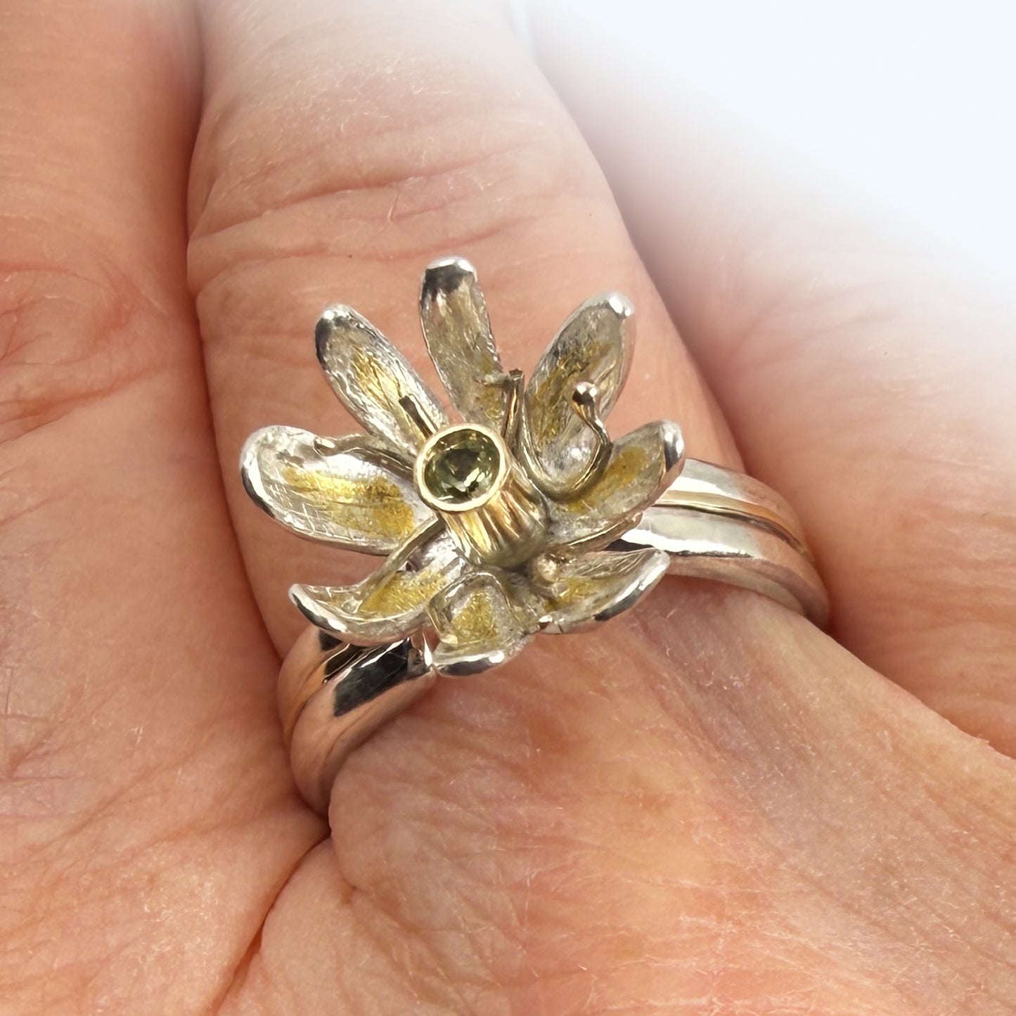 Expanded Skies Dartmoor Celandine Sapphire Ring celebrates the beauty of the waysides and meadows, radiant with wild yellow celandines (Ficaria verna).

The ring is totally handcrafted on the edge of Dartmoor. The band is made from sterling silver, inlaid on the shoulders with 9ct gold.

The flower is made from fine silver with 24ct gold accents fused to the surface of the petals. The celandine has a 9ct gold setting for the beautiful ethically sourced yellow-green sapphire, that really captures the colours