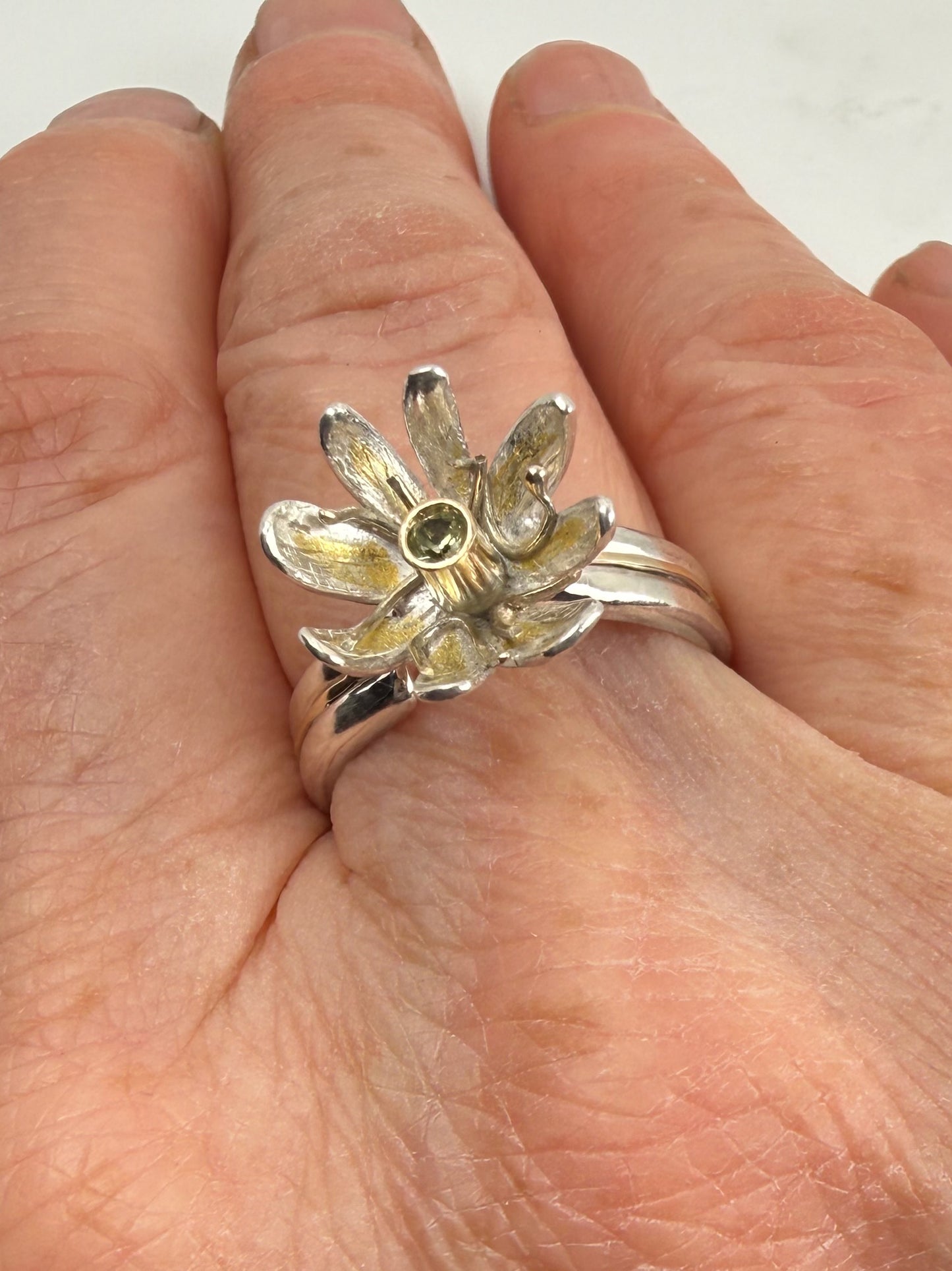 Expanded Skies Dartmoor Celandine Sapphire Ring celebrates the beauty of the waysides and meadows, radiant with wild yellow celandines (Ficaria verna).

The ring is totally handcrafted on the edge of Dartmoor. The band is made from sterling silver, inlaid on the shoulders with 9ct gold.

The flower is made from fine silver with 24ct gold accents fused to the surface of the petals. The celandine has a 9ct gold setting for the beautiful ethically sourced yellow-green sapphire, that really captures the colours