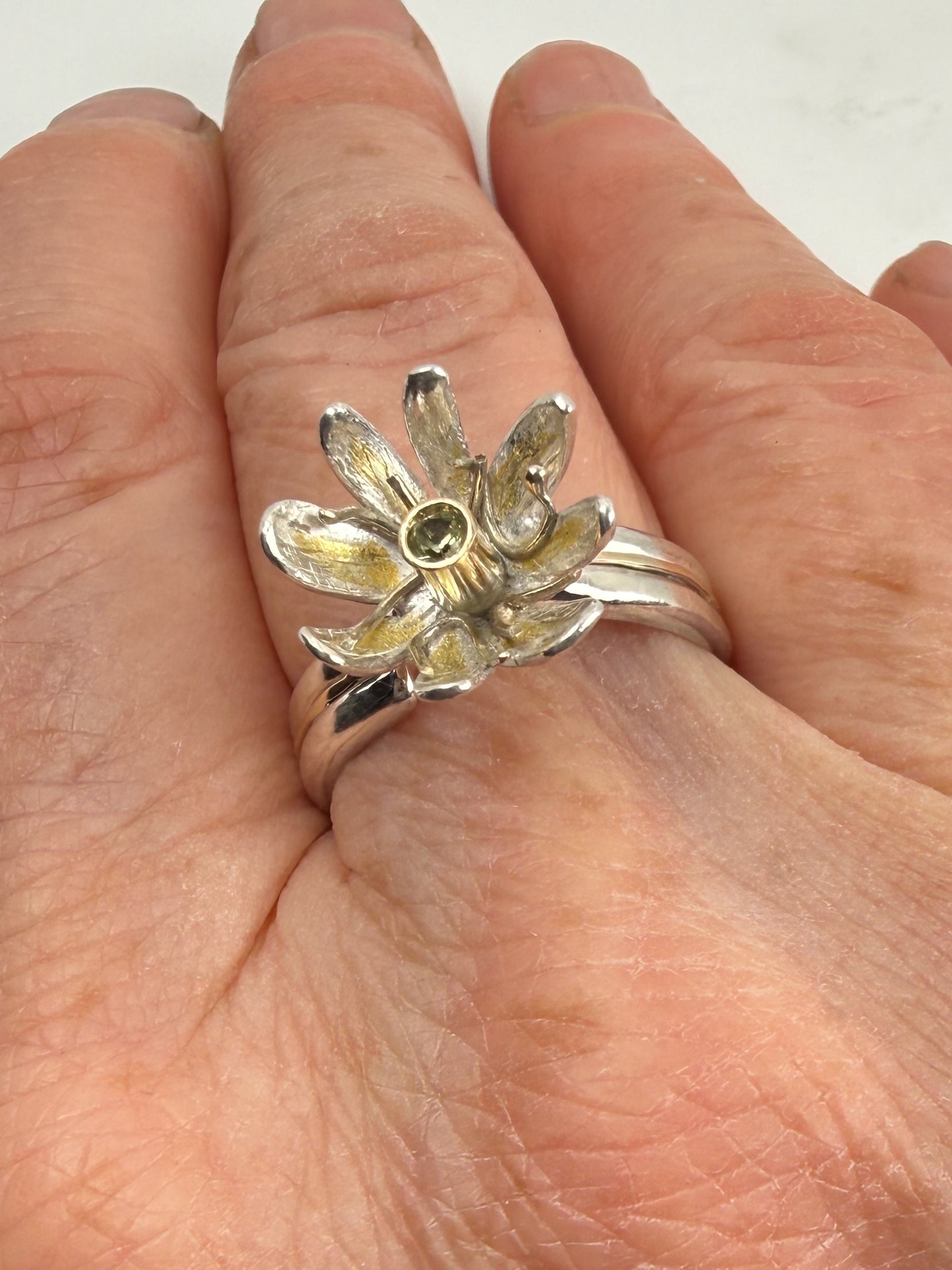 Expanded Skies Dartmoor Celandine Sapphire Ring celebrates the beauty of the waysides and meadows, radiant with wild yellow celandines (Ficaria verna).

The ring is totally handcrafted on the edge of Dartmoor. The band is made from sterling silver, inlaid on the shoulders with 9ct gold.

The flower is made from fine silver with 24ct gold accents fused to the surface of the petals. The celandine has a 9ct gold setting for the beautiful ethically sourced yellow-green sapphire, that really captures the colours