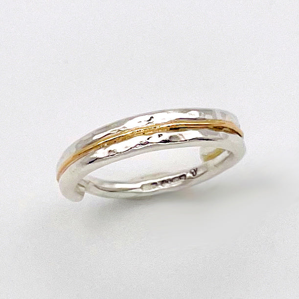 The Expanded Skies Dartmoor Dart Valley Hammered Ring, inlaid with 9ct Gold, is inspired by the River Dart, that viewed from high on top of granite moorland, glints and snakes through the steep sides of the deeply wooded valley. The hammered band is handcrafted from a single band of sold sterling recycled silver at back that flows into a recycled 9ct gold band at the front, flanked by two silver bands.