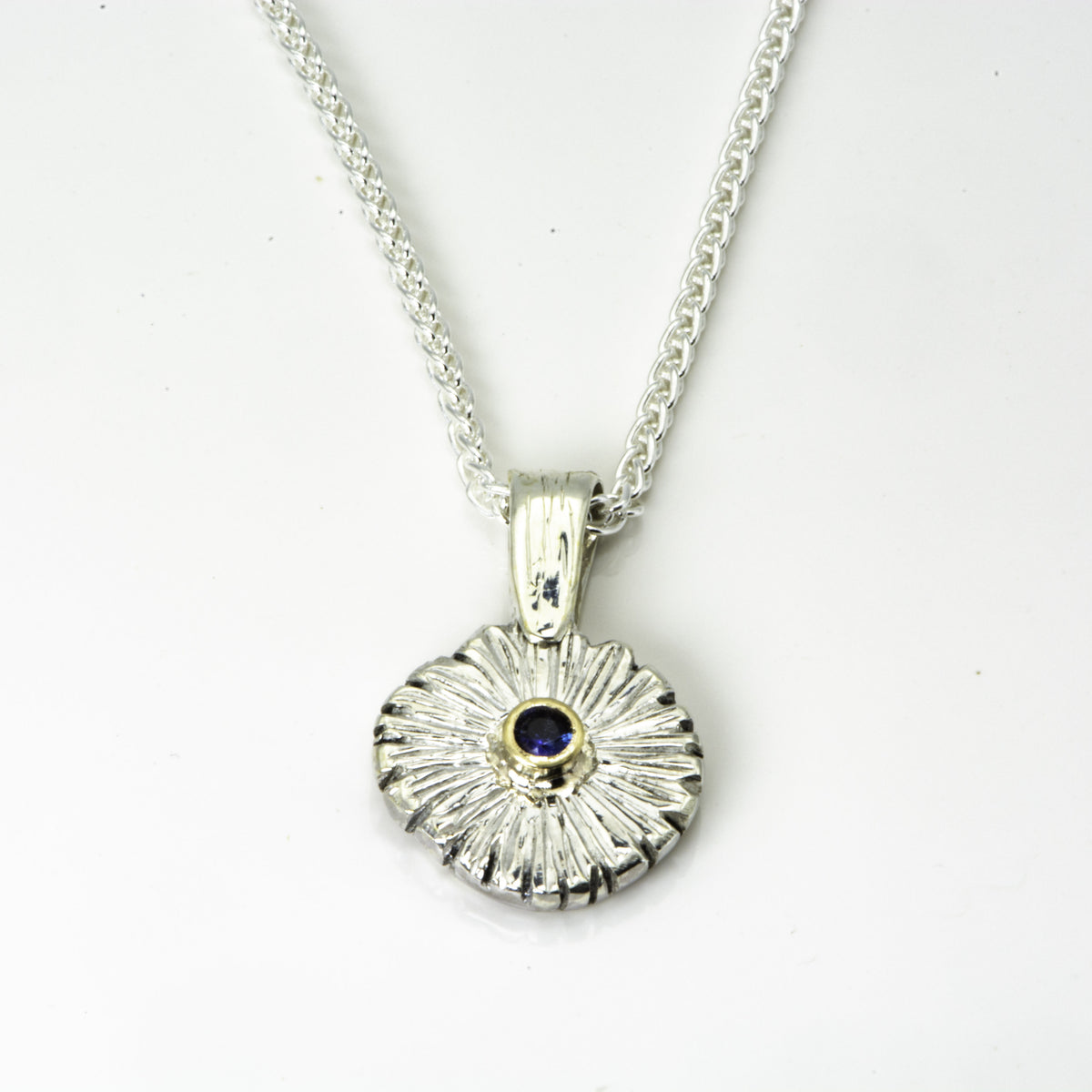 The Expanded Skies Dartmoor Daisy Blue Sapphire Necklace in sterling silver and 9ct gold is inspired by the Erigeron Karvinskianus, commonly known as the 'Dartmoor Daisy'. It comes with 16” Italian spiga rolled chain, made from recycled sterling silver. The daisy pendant measures 12mm, the bail measures 6mm, total length 18mm with a depth of 2mm (approx). Each piece is individually saw pierced, hand engraved and
unique. The ethically sourced 2.5mm is a beautiful brilliant blue, facetted Sri Lankan sapphire,
