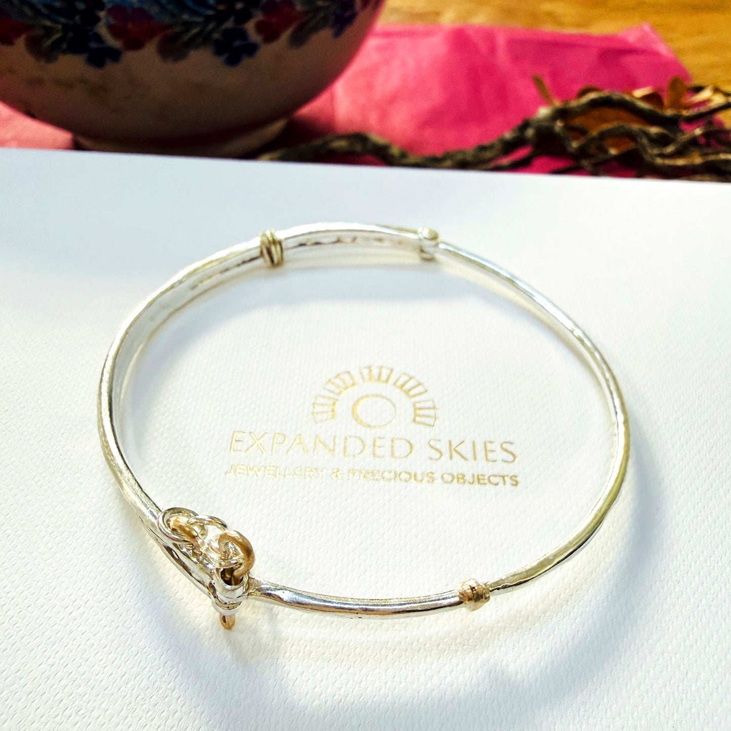 The River Dart at Hembury Hinged Bangle evokes the River Dart that flows through Hembury Woods, where the water eddies and glints as it swirls around the rocks. 
The bangle is totally handcrafted on the edge of Dartmoor and made from high quality recycled sterling silver, inlaid with recycled 9ct gold, with a textured finish that reflects the light. Shown with Expanded Skies box handcrafted in Cornwall.