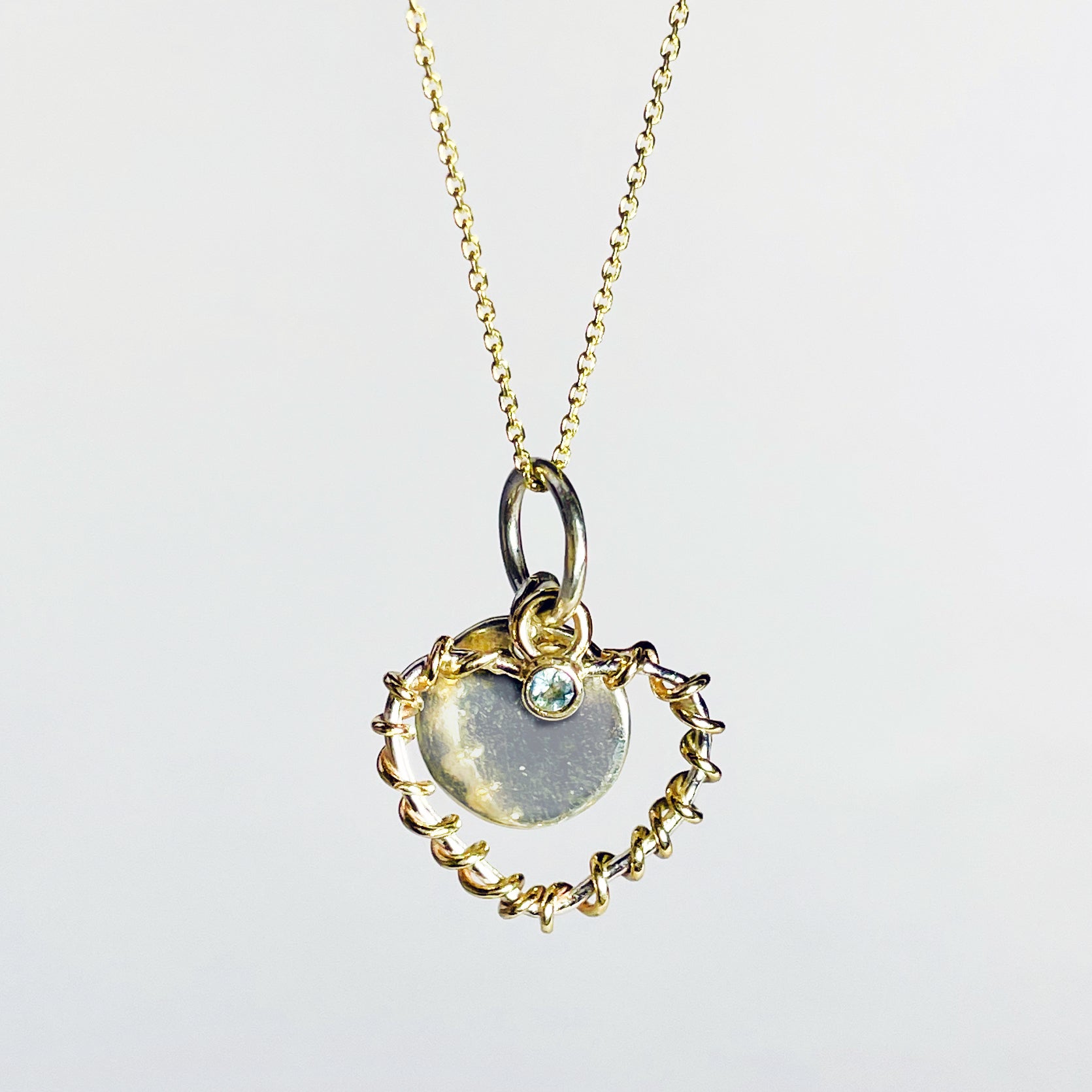 Expanded Skies Sapphire Sky Blue Heart Pendant has a beautiful ethically sourced Sri Lankan mid blue faceted sapphire set in 9ct gold on a silver heart wound with 9ct gold accompanied by a small silver disk. Totally handcrafted on the edge of Dartmoor and made from high quality recycled sterling silver and recycled gold. 