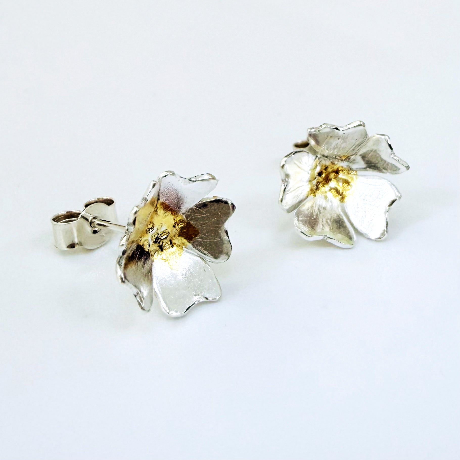 The Expanded Skies Dartmoor Field Rose Studs captures the joyous simple beauty of the field rose, Rosa arvensis, that is seen weaving brightly through the Dartmoor hedgerows and woodland.
Handcrafted in recycled fine silver with recycled 24ct gold accents and recycled sterling silver ear pins and scrolls.