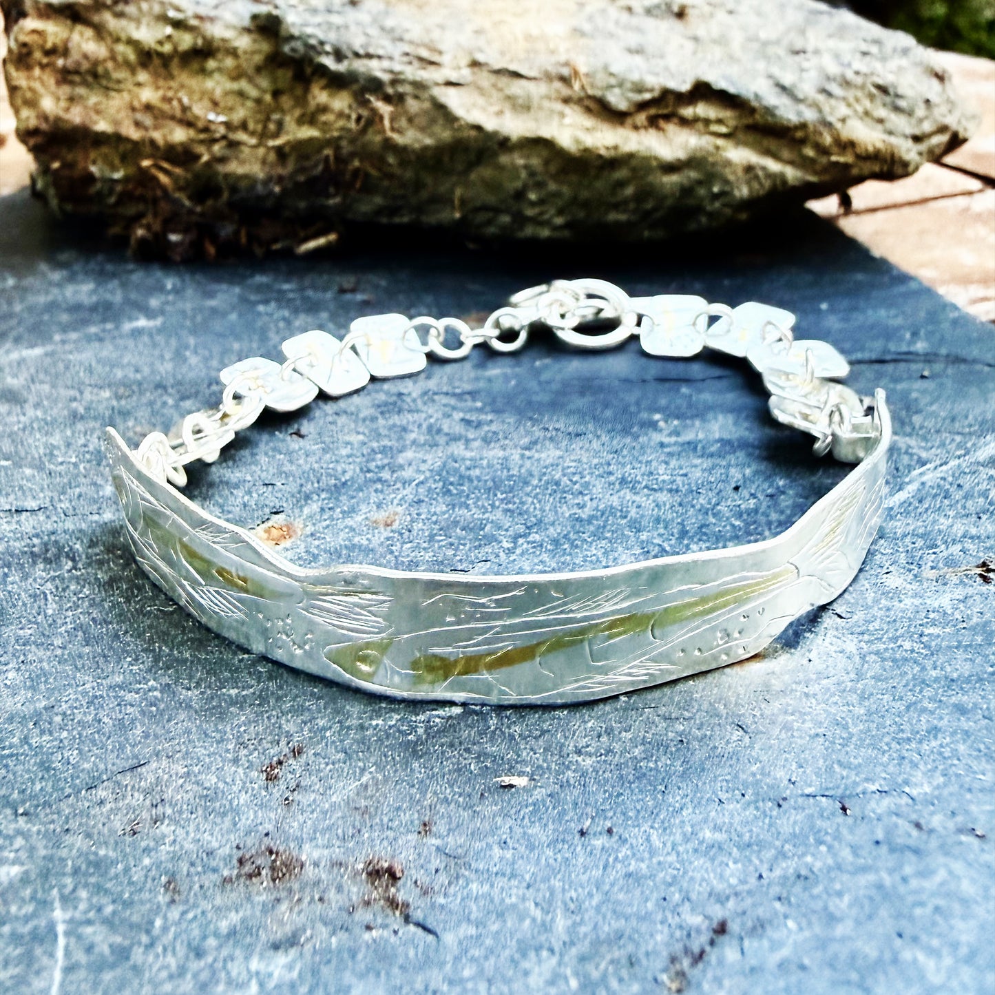 The Expanded Skies Dartmoor minnows bracelet captures the graceful beauty of the minnows as they somersault through the glistening River Dart at Hembury Woods, created in fine and sterling silver with 24ct gold accents. The chain is created with hand engraved fine silver panels with 24ct gold accents depict the moving river. Understated and beautiful, it can be worn every day or for special occasions, for men and women.The bracelet is totally handcrafted on the edge of Dartmoor from recycled precious metals