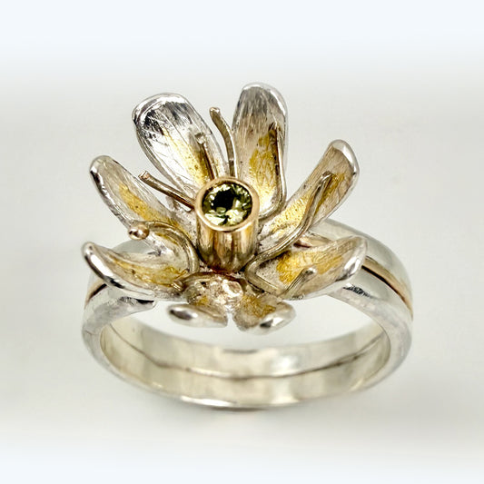 Expanded Skies Dartmoor Celandine Sapphire Ring celebrates the beauty of the waysides and meadows, radiant with wild yellow celandines (Ficaria verna).

The ring is totally handcrafted on the edge of Dartmoor. The band is made from sterling silver, inlaid on the shoulders with 9ct gold.

The flower is made from fine silver with 24ct gold accents fused to the surface of the petals. The celandine has a 9ct gold setting for the beautiful ethically sourced yellow-green sapphire, that really captures the colours
