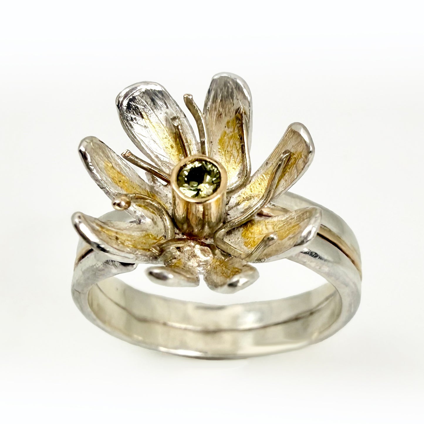 Expanded Skies Dartmoor Celandine Sapphire Ring celebrates the beauty of the waysides and meadows, radiant with wild yellow celandines (Ficaria verna).

The ring is totally handcrafted on the edge of Dartmoor. The band is made from sterling silver, inlaid on the shoulders with 9ct gold.

The flower is made from fine silver with 24ct gold accents fused to the surface of the petals. The celandine has a 9ct gold setting for the beautiful ethically sourced yellow-green sapphire, that really captures the colours