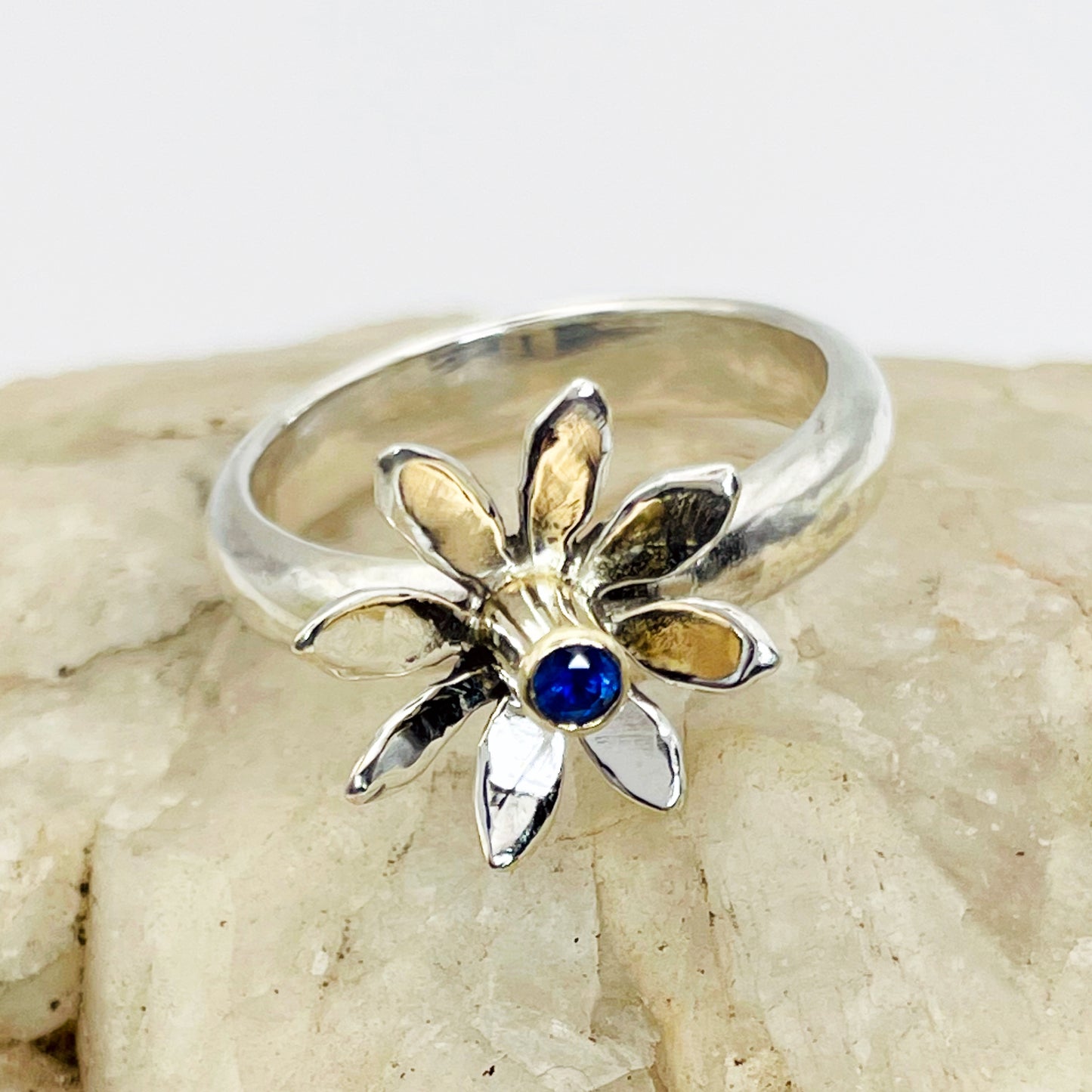 The Expanded Skies Breeze Blown Daisy Sapphire Ring is joyful! A beautiful brilliant bright blue, ethically sourced, Sri Lankan sapphire is set in solid 9ct gold that reflects onto to the high polish recycled silver petals, giving a sense of movement. The ring is totally handcrafted on the edge of Dartmoor.