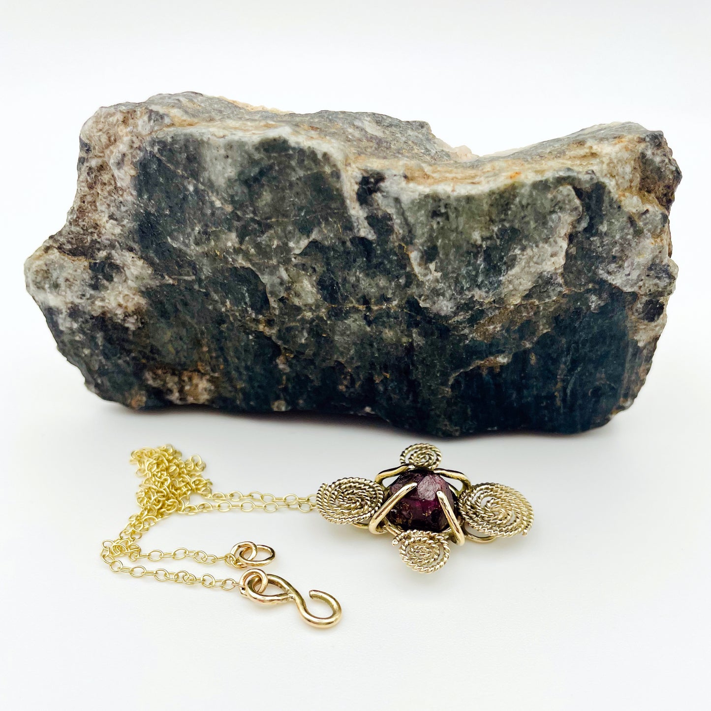 The Expanded Skies Raw Garnet Spiral Filigree Necklace has a beautiful raw Norwegian garnet set in 9ct gold. The garnet is set in a distinctive completely handcrafted 9ct gold filigree and claw setting. It features the neolithic symbol of the spiral, representing the life force and the cycles of life. This is a unique piece, one-of-a-kind. Handcrafted on the edge of Dartmoor and made from high quality recycled gold, Hallmarked by the London Assay Office.