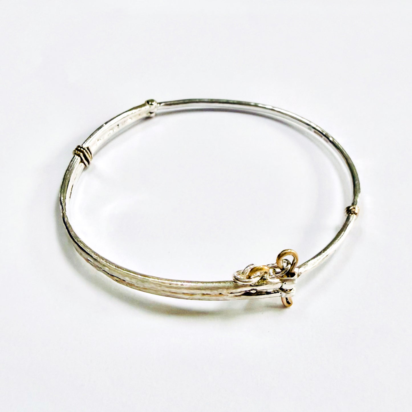 The River Dart at Hembury Hinged Bangle evokes the River Dart that flows through Hembury Woods, where the water eddies and glints as it swirls around the rocks. 
The bangle is totally handcrafted on the edge of Dartmoor and made from high quality recycled sterling silver, inlaid with recycled 9ct gold, with a textured finish that reflects the light. 