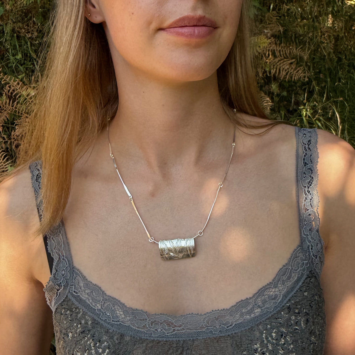 The Expanded Skies Dartmoor Wild Honeysuckle Leaves Necklace is a hand engraved of the graceful honeysuckle (Lonicera periclymenum) as it winds through the trees and brambles in Ausewell Woods. Handcrafted in fine silver with 24ct gold accents, with a completely handcrafted stem and tendril chain in sterling silver. Simple and elegant with a polished finish, it can be worn everyday for any occasion. Pictured on woman