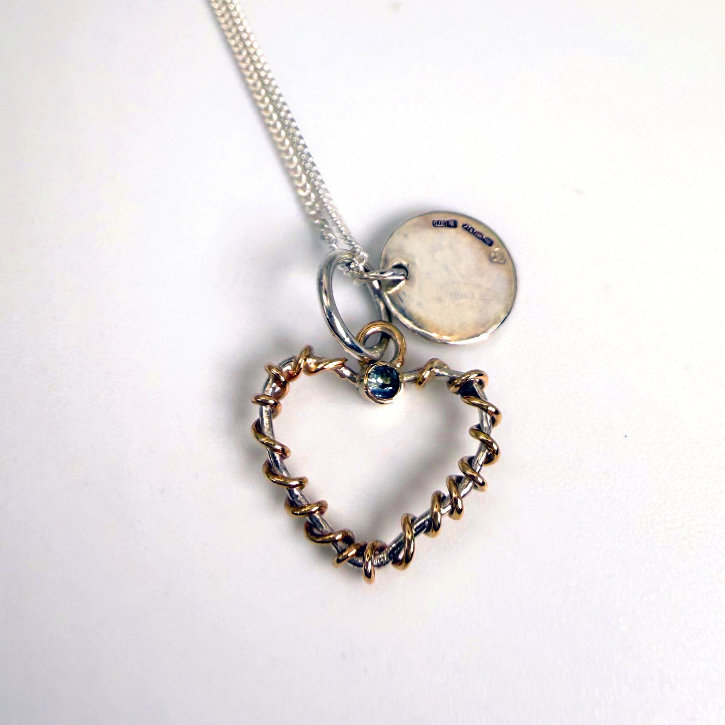 Expanded Skies Sapphire Sky Blue Heart Pendant has a beautiful ethically sourced Sri Lankan mid blue faceted sapphire set in 9ct gold on a silver heart wound with 9ct gold accompanied by a small silver disk. Totally handcrafted on the edge of Dartmoor and made from high quality recycled sterling silver and recycled gold. 