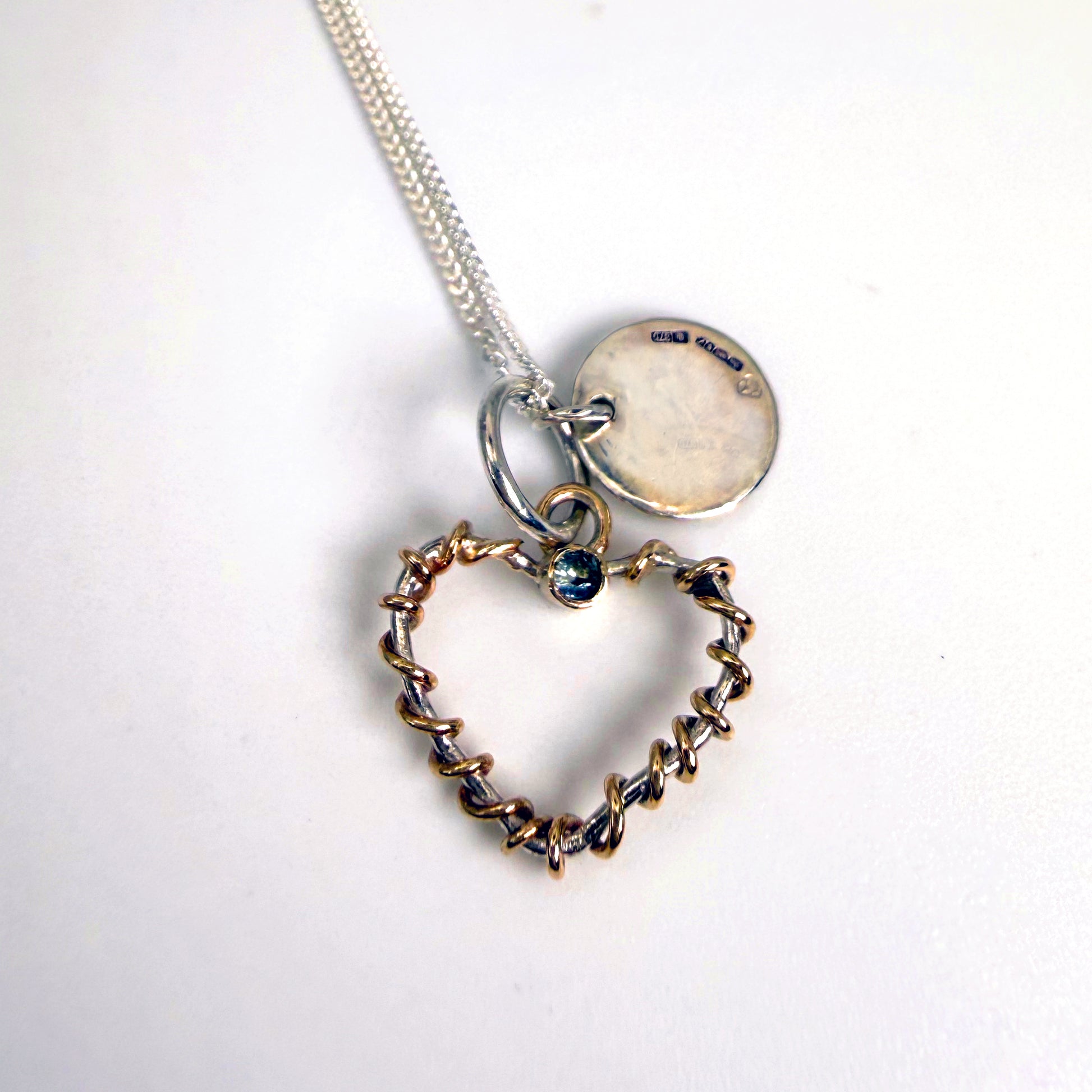 Expanded Skies Sapphire Sky Blue Heart Pendant has a beautiful ethically sourced Sri Lankan mid blue faceted sapphire set in 9ct gold on a silver heart wound with 9ct gold accompanied by a small silver disk. Totally handcrafted on the edge of Dartmoor and made from high quality recycled sterling silver and recycled gold. 