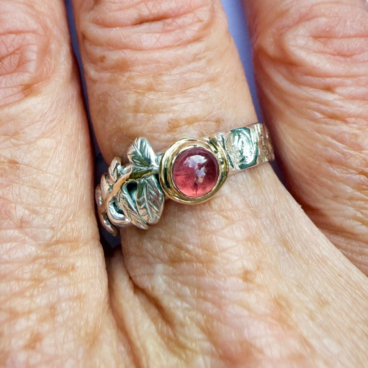 
Expanded Skies Dartmoor Rowan Leaf and Berries Spinel Ring. The Expanded Skies Dartmoor Rowan Leaf and Berries Spinel Ring is totally handcrafted on the edge of Dartmoor. The ring is created in recycled sterling silver, inlaid with 9ct gold. The ring is set with an ethically sourced Tanzanian red-pink spinel, set in 9ct gold, with a hand formed rowan leaf, inlaid with 9ct gold. The ethically sourced 4.5mm round spinel is from Moyo Gems. Moyo gems is run by female miners Tanzanian Women Miners' Association.