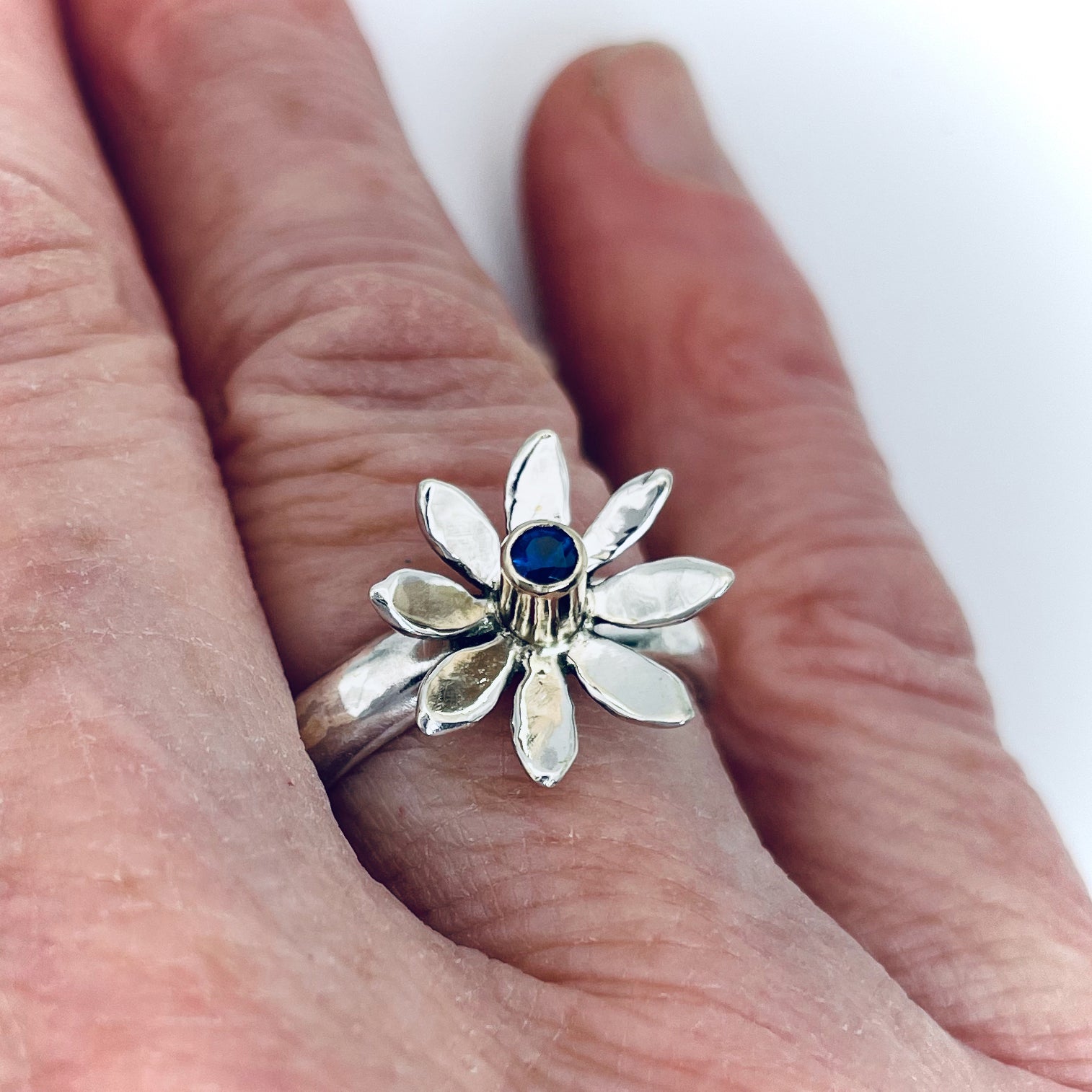 The Expanded Skies Breeze Blown Daisy Sapphire Ring is joyful! A beautiful brilliant bright blue, ethically sourced, Sri Lankan sapphire is set in solid 9ct gold that reflects onto to the high polish recycled silver petals, giving a sense of movement. The ring is totally handcrafted on the edge of Dartmoor.