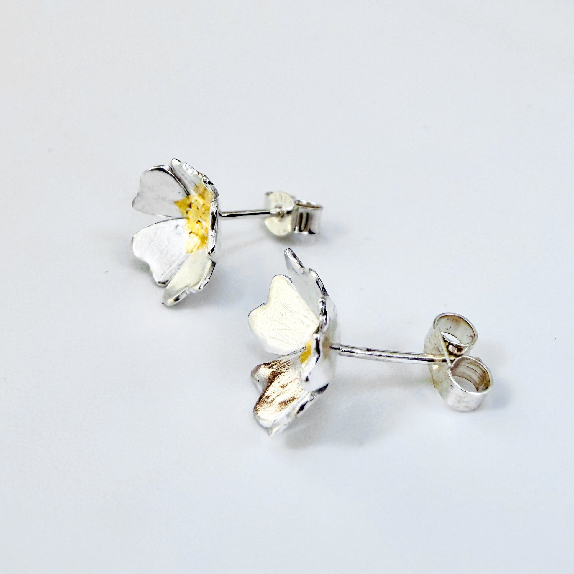 The Expanded Skies Dartmoor Field Rose Studs captures the joyous simple beauty of the field rose, Rosa arvensis, that is seen weaving brightly through the Dartmoor hedgerows and woodland.
Handcrafted in recycled fine silver with recycled 24ct gold accents and recycled sterling silver ear pins and scrolls.