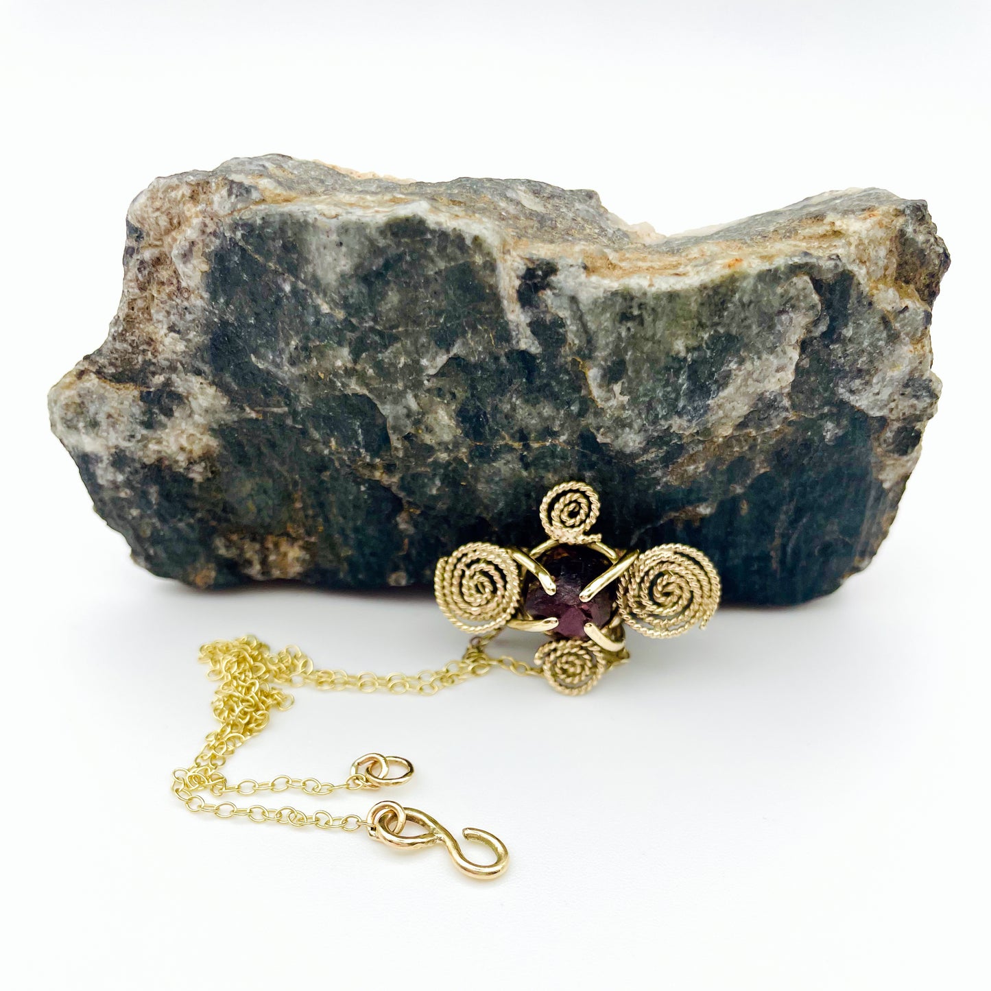 The Expanded Skies Raw Garnet Spiral Filigree Necklace has a beautiful raw Norwegian garnet set in 9ct gold. The garnet is set in a distinctive completely handcrafted 9ct gold filigree and claw setting. It features the neolithic symbol of the spiral, representing the life force and the cycles of life. This is a unique piece, one-of-a-kind. Handcrafted on the edge of Dartmoor and made from high quality recycled gold, Hallmarked by the London Assay Office.