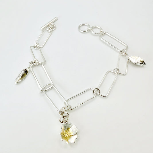 The Expanded Skies Dartmoor Field Rose Bracelet captures the joyous beauty of the field rose, Rosa arvensis, seen weaving brightly through the Dartmoor hedgerows and woodland. The bracelet’s rose and leaves are hand engraved and has a painterly feel, accented with 24ct gold.