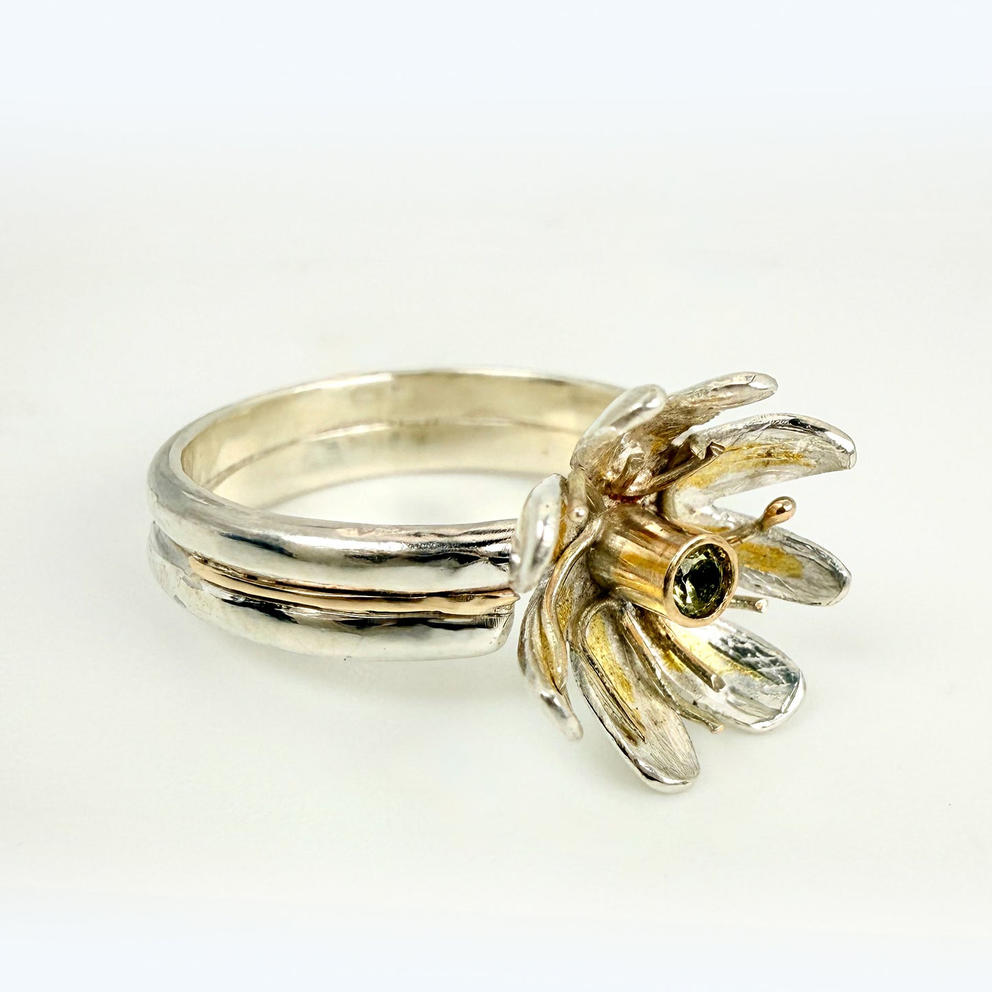 Expanded Skies Dartmoor Celandine Sapphire Ring celebrates the beauty of the waysides and meadows, radiant with wild yellow celandines (Ficaria verna).

The ring is totally handcrafted on the edge of Dartmoor. The band is made from sterling silver, inlaid on the shoulders with 9ct gold.

The flower is made from fine silver with 24ct gold accents fused to the surface of the petals. The celandine has a 9ct gold setting for the beautiful ethically sourced yellow-green sapphire, that really captures the colours