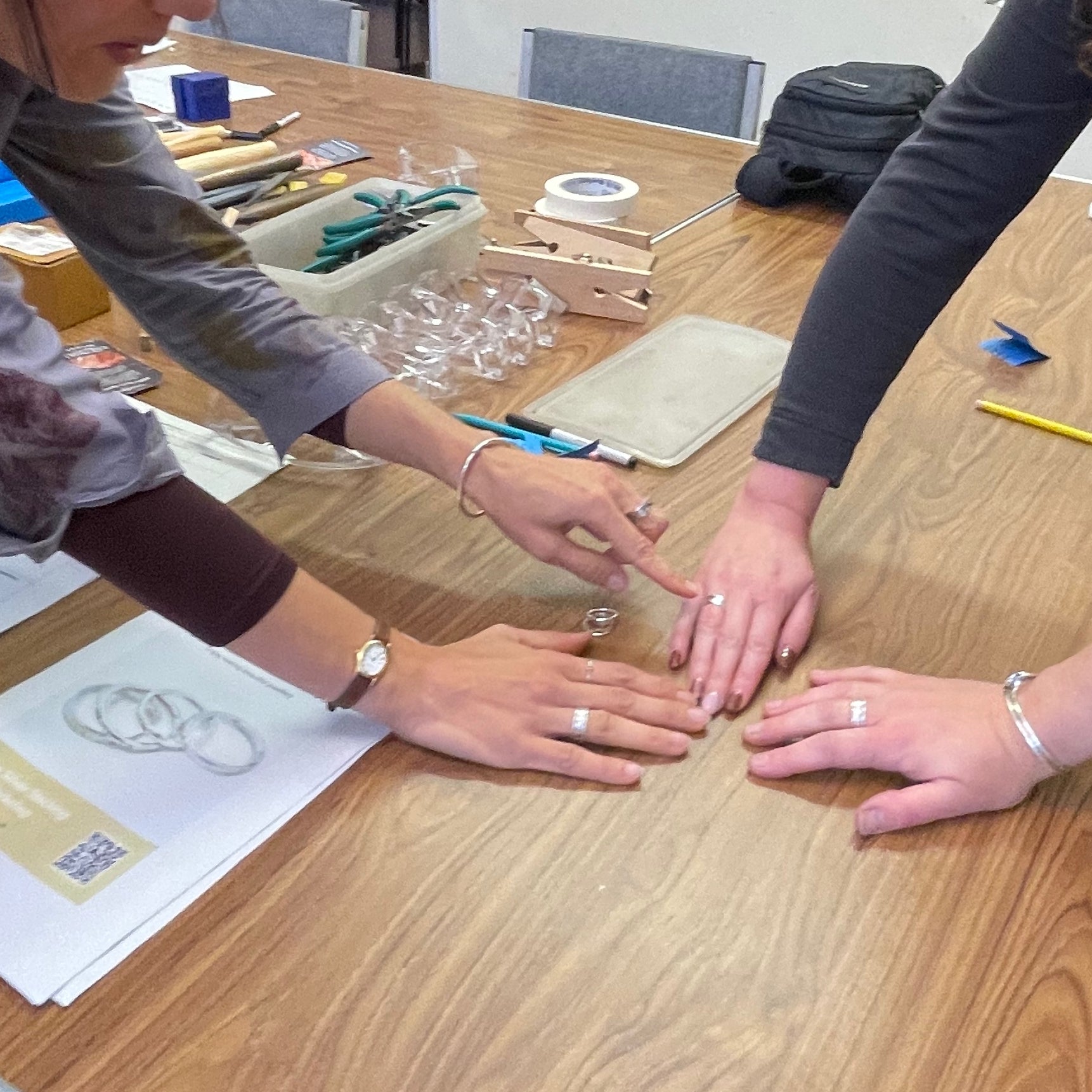 6 December 2025 Ashburton Jewellery School - Make Three Sterling Silver Stacking Rings- Two people with rings on their fingers showing rings they have made with tools and materials.