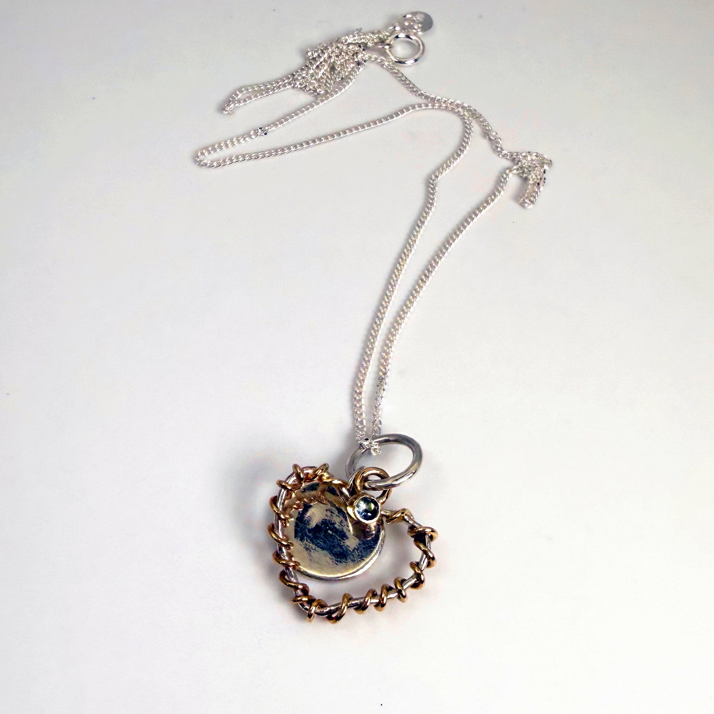 Expanded Skies Sapphire Sky Blue Heart Pendant has a beautiful ethically sourced Sri Lankan mid blue faceted sapphire set in 9ct gold on a silver heart wound with 9ct gold accompanied by a small silver disk. Totally handcrafted on the edge of Dartmoor and made from high quality recycled sterling silver and recycled gold. 