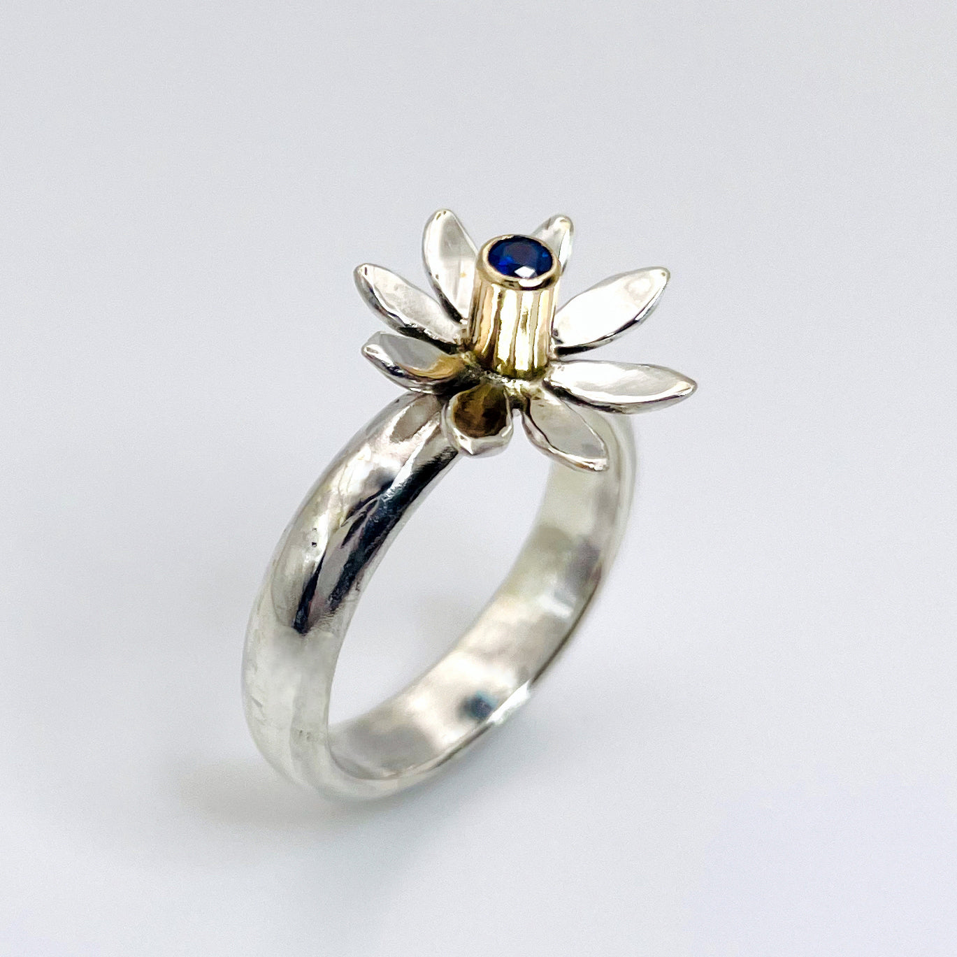 The Expanded Skies Breeze Blown Daisy Sapphire Ring is joyful! A beautiful brilliant bright blue, ethically sourced, Sri Lankan sapphire is set in solid 9ct gold that reflects onto to the high polish recycled silver petals, giving a sense of movement. The ring is totally handcrafted on the edge of Dartmoor.