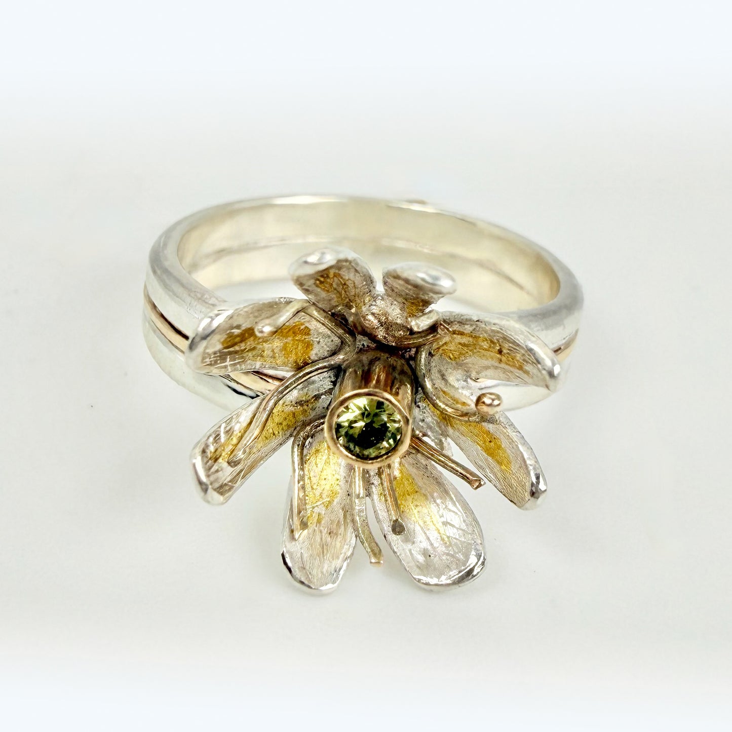 Expanded Skies Dartmoor Celandine Sapphire Ring celebrates the beauty of the waysides and meadows, radiant with wild yellow celandines (Ficaria verna).

The ring is totally handcrafted on the edge of Dartmoor. The band is made from sterling silver, inlaid on the shoulders with 9ct gold.

The flower is made from fine silver with 24ct gold accents fused to the surface of the petals. The celandine has a 9ct gold setting for the beautiful ethically sourced yellow-green sapphire, that really captures the colours