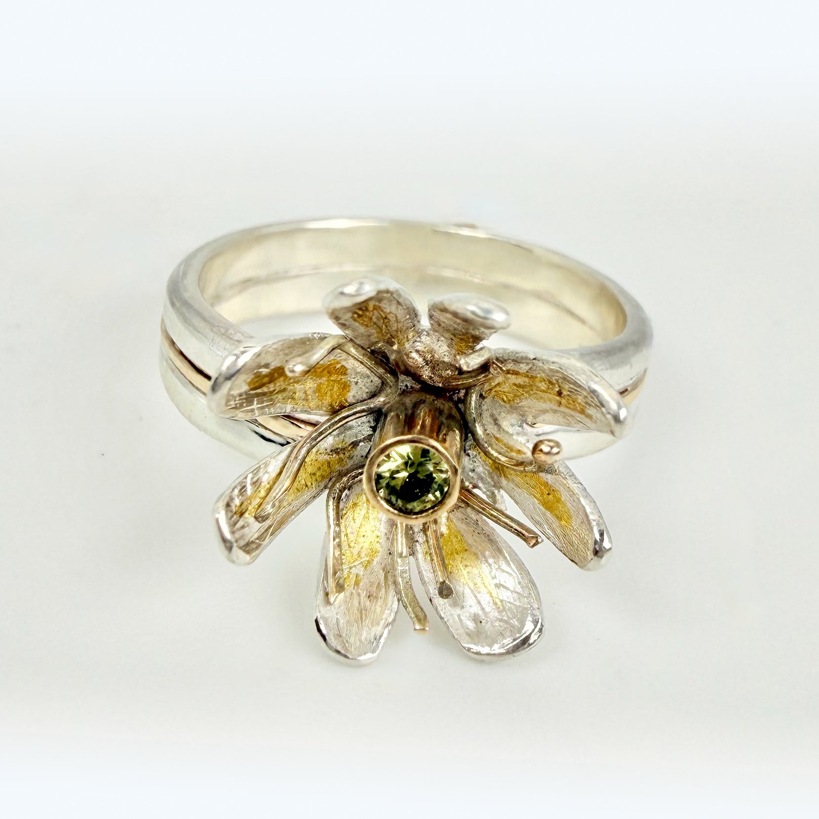 Expanded Skies Dartmoor Celandine Sapphire Ring celebrates the beauty of the waysides and meadows, radiant with wild yellow celandines (Ficaria verna).

The ring is totally handcrafted on the edge of Dartmoor. The band is made from sterling silver, inlaid on the shoulders with 9ct gold.

The flower is made from fine silver with 24ct gold accents fused to the surface of the petals. The celandine has a 9ct gold setting for the beautiful ethically sourced yellow-green sapphire, that really captures the colours